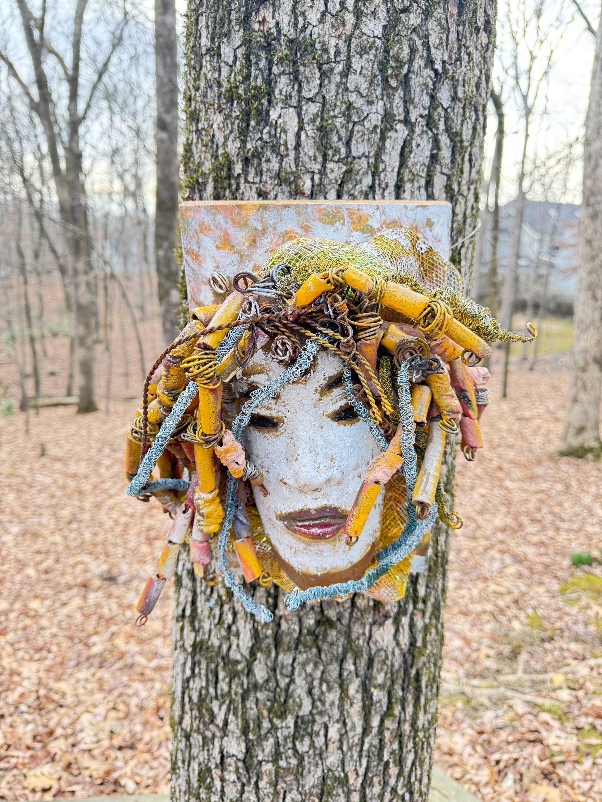 Experience the unique beauty of Amos, a mixed media raku fire mask carefully crafted with over 50 handmade beads and 50 feet of 24 and 16 gauge wire. Mounted on a 7” x 12” wood board and weighing approximately 4 pounds, Amos features an off-white face with braided and beaded  hair. This one-of-a-kind masterpiece also includes several fabrics of netting in his hair, making it larger than most masks.