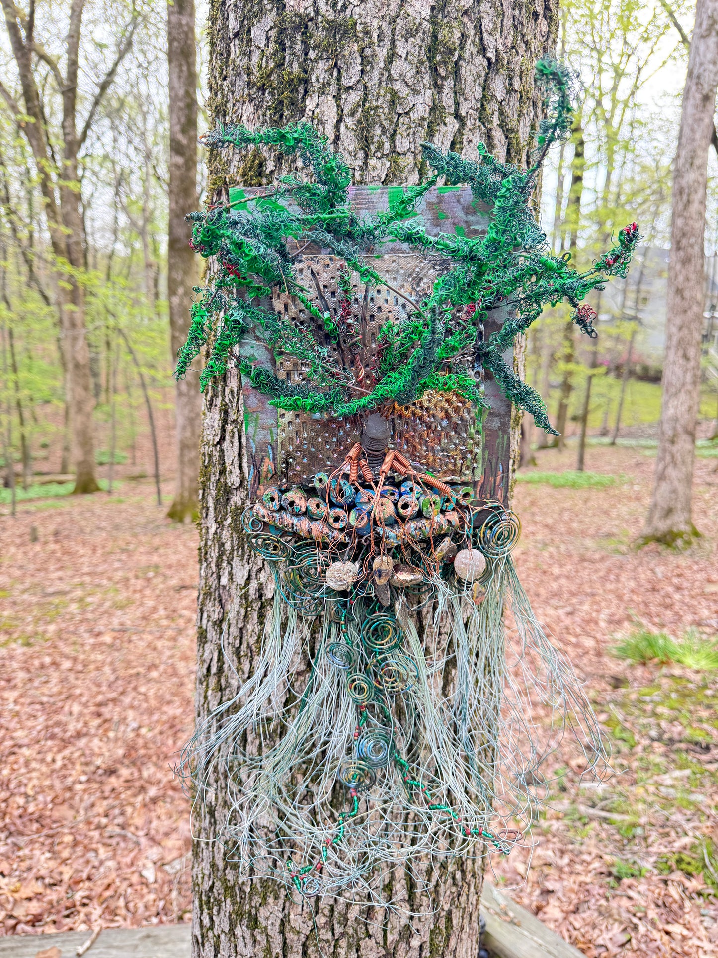 Explore the mesmerizing coil root of The Radiant Root, a mystical subterranean world showcased on a 20"x16" canvas embellished with a combination of 16- and 24-gauge wire and exquisite Raku fire beads, alongside a captivating RAKU fired and hand-painted texture tile resting on a 7"x5" wooden base, with a weight of 1.8 lbs. Immerse yourself in the vibrant shades of a summer sunset as the sunlight highlights the lush greenery.
