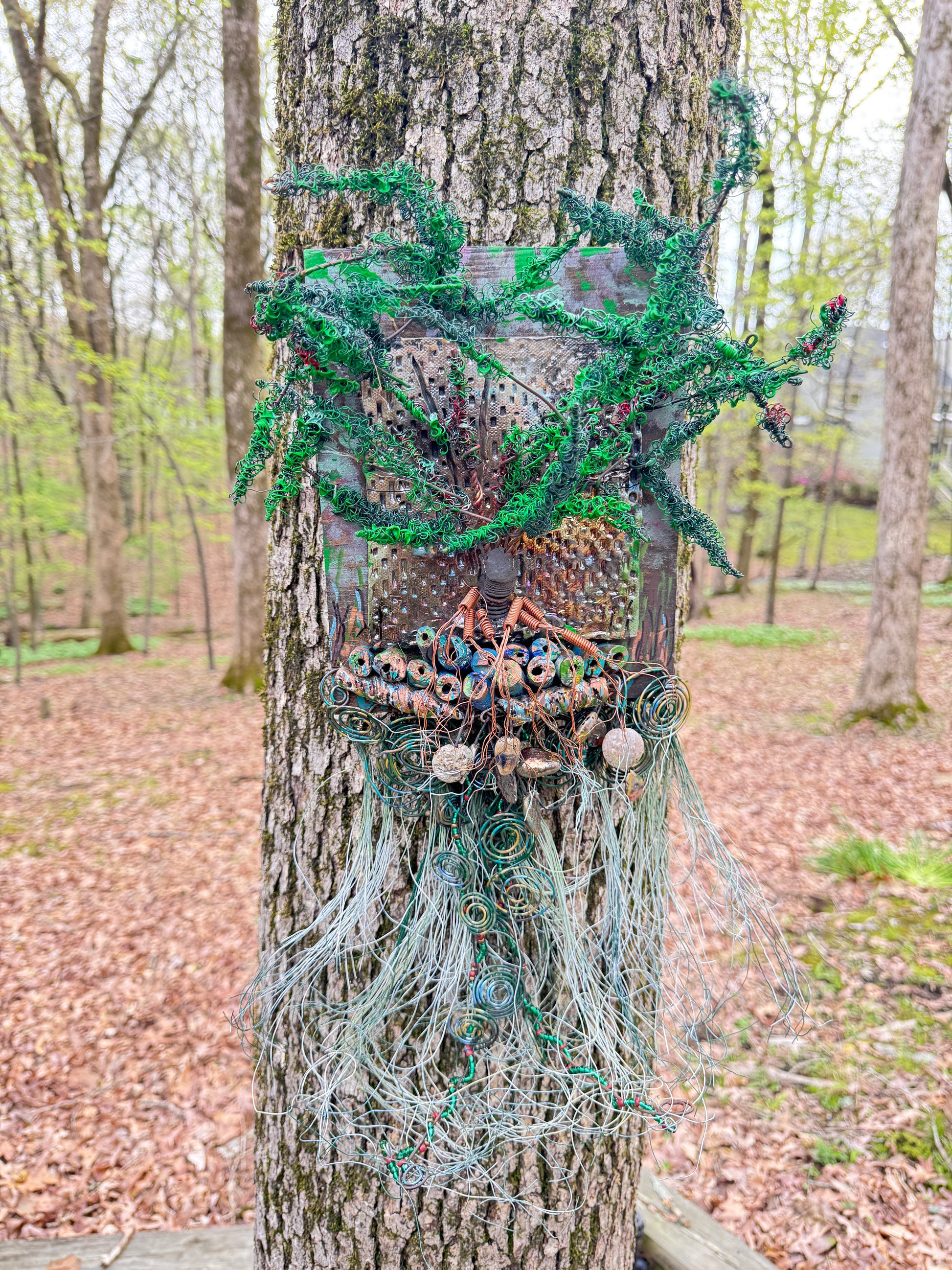 Explore the mesmerizing coil root of The Radiant Root, a mystical subterranean world showcased on a 20"x16" canvas embellished with a combination of 16- and 24-gauge wire and exquisite Raku fire beads, alongside a captivating RAKU fired and hand-painted texture tile resting on a 7"x5" wooden base, with a weight of 1.8 lbs. Immerse yourself in the vibrant shades of a summer sunset as the sunlight highlights the lush greenery.