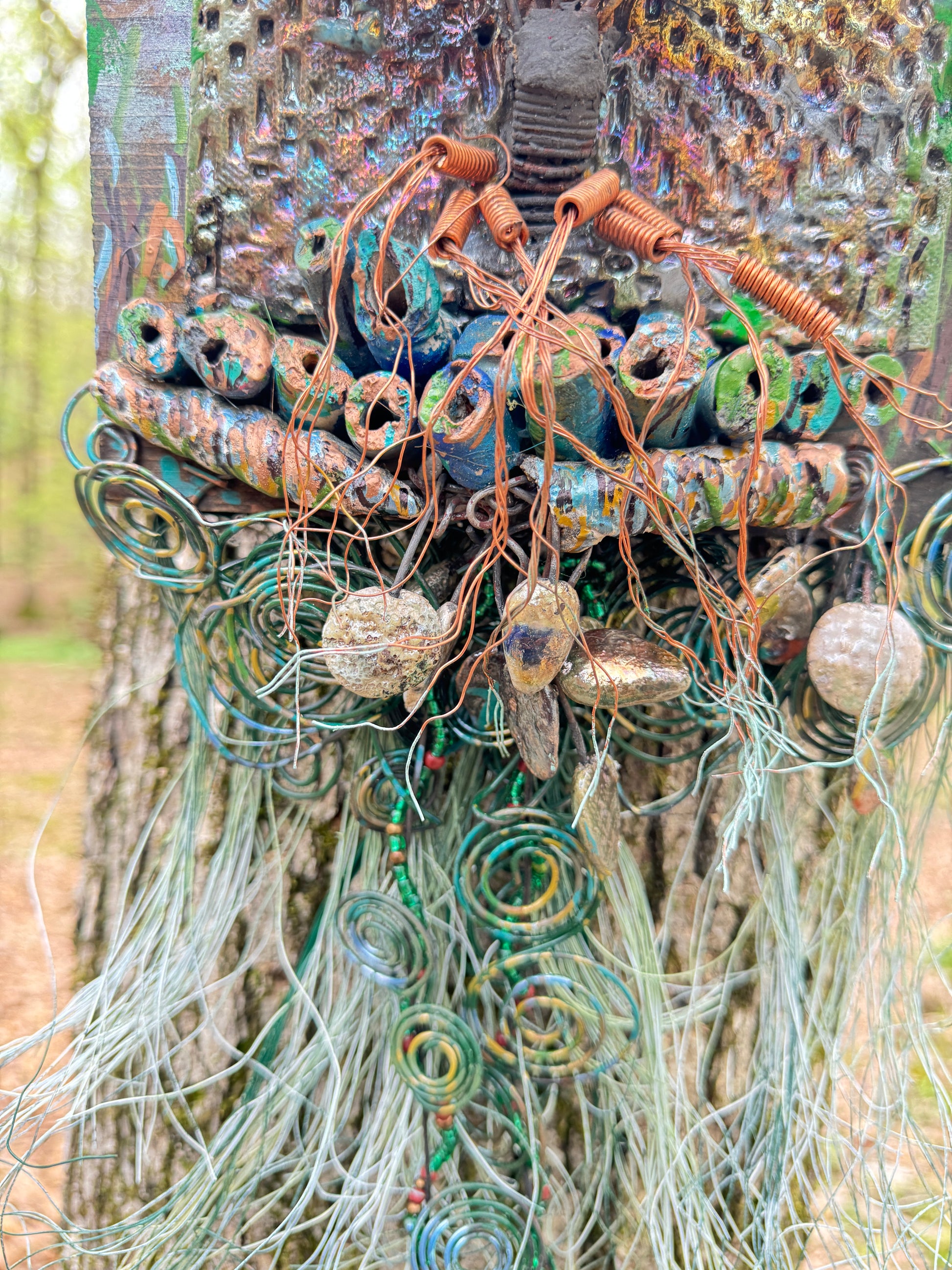 Explore the mesmerizing coil root of The Radiant Root, a mystical subterranean world showcased on a 20"x16" canvas embellished with a combination of 16- and 24-gauge wire and exquisite Raku fire beads, alongside a captivating RAKU fired and hand-painted texture tile resting on a 7"x5" wooden base, with a weight of 1.8 lbs. Immerse yourself in the vibrant shades of a summer sunset as the sunlight highlights the lush greenery.