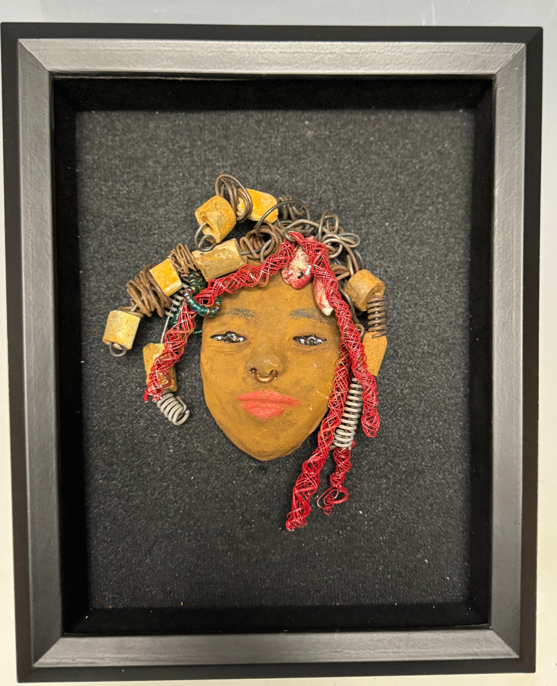 At 5" x 6" in size, Ola makes a stunning addition to walls, trees, and shadow boxes. His signature red braided hair is ornamented with handcrafted Raku beads, while his skin has a warm honey brown hue. Each piece is equipped with over 20 feet of top-notch 16 & 24-gauge wire in the hair. This fashionable sculpture will bring a modern flair to any room - simply place it in a shadow box and enjoy!