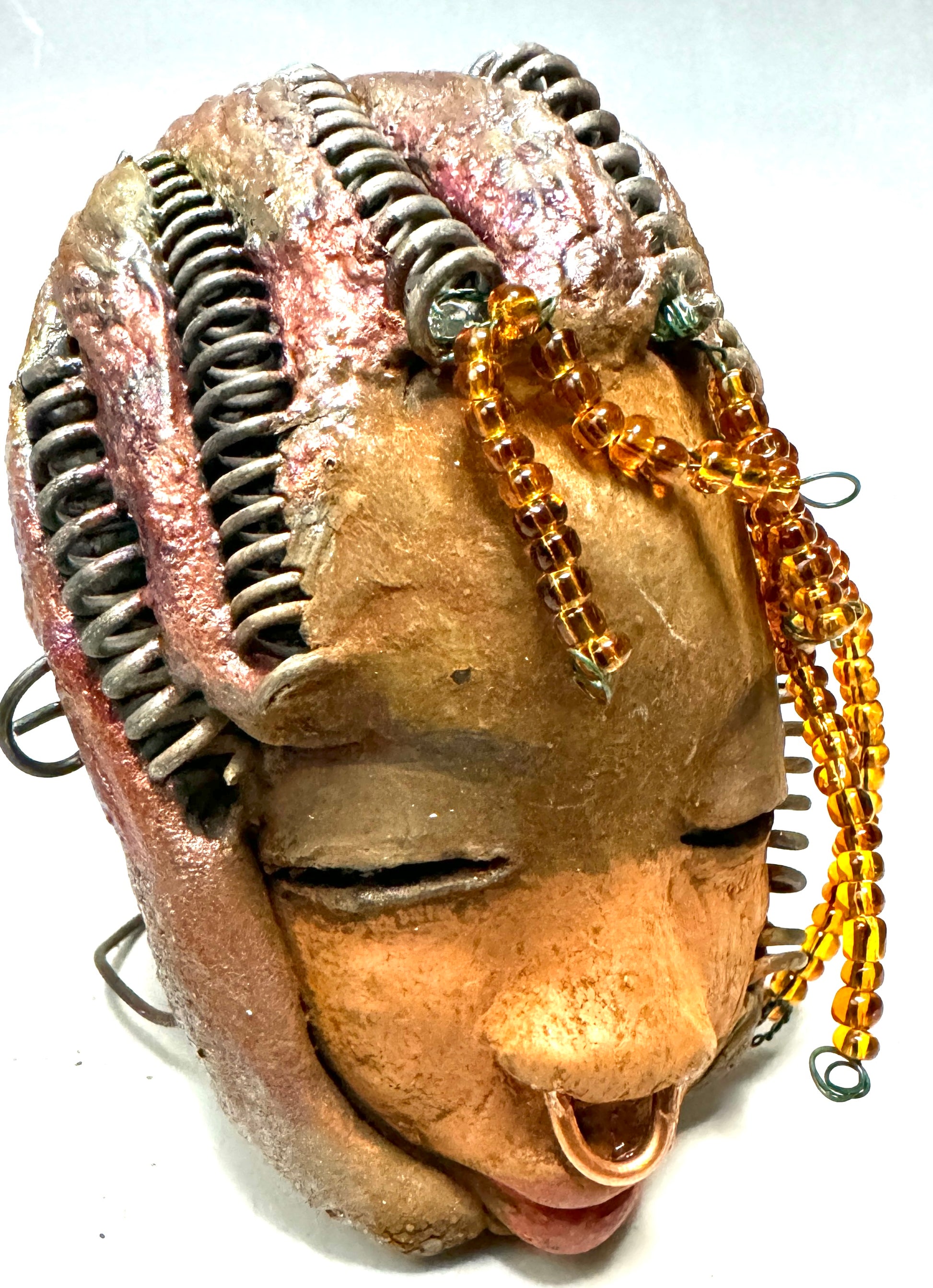 Kenya weighs 5 oz and is 4" by 3" in diameter. Her hair is coppered braided, her complexion is a light gray-blue, and her lips are black. She is a perfect item to start with from the HerDew mask collection. Shadowbox not included.