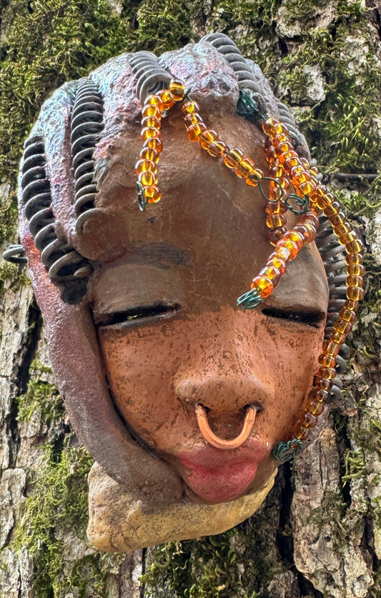 Kenya weighs 5 oz and is 4" by 3" in diameter. Her hair is coppered braided, her complexion is a light gray-blue, and her lips are black. She is a perfect item to start with from the HerDew mask collection. Shadowbox not included.