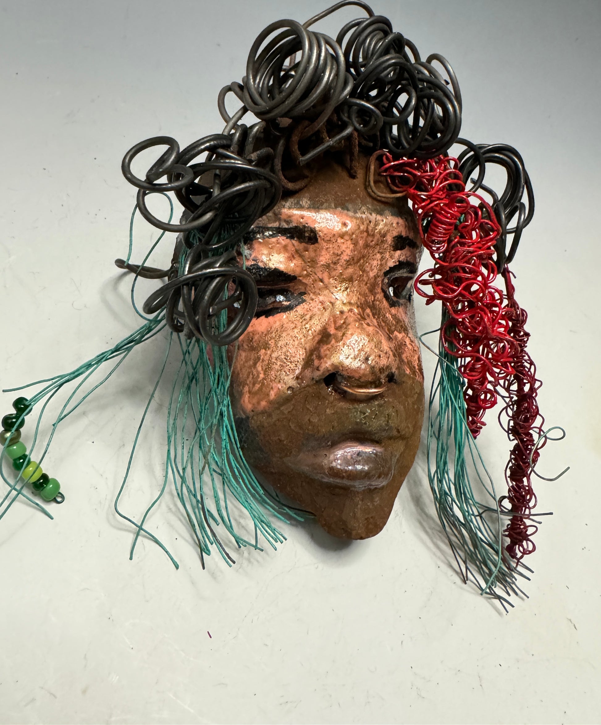 Dakari is an eye-catching two tone tribal raku mask, measuring 4 x 7" and weighing 6 oz. This mask is finished with a stunning blue  and red hair. Dakari also features a copper nose ring. Shadowbox is not included.