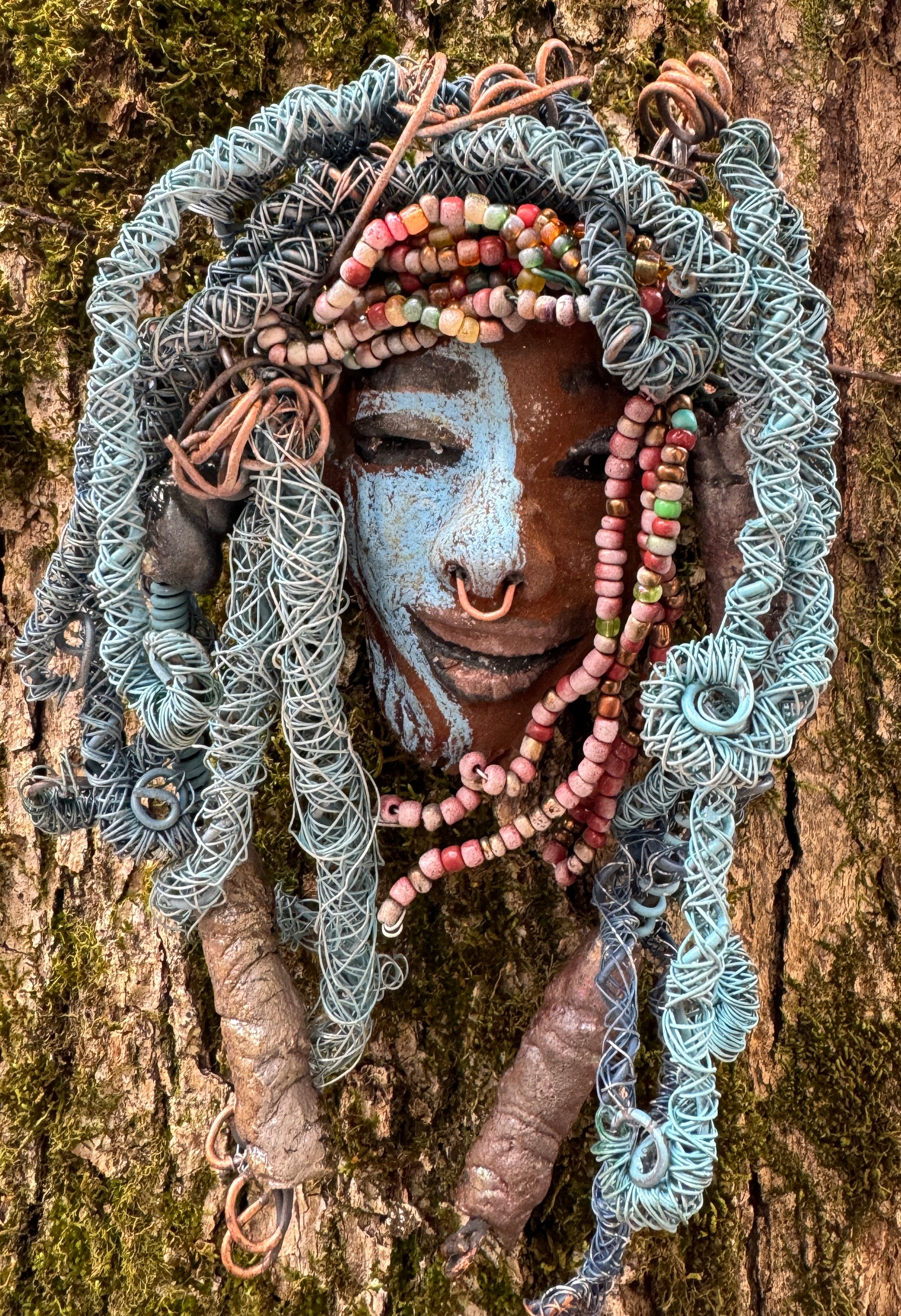 Zola is a mesmerizing raku mask with a captivating tribal face. She measures approximately 5 x 9" and weighs 7 oz. The mask is further decorated with blue hair and a copper nose ring.