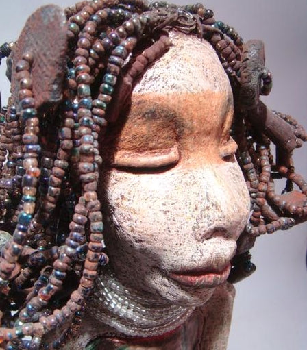 Meet Ariel, a meticulously crafted beauty. Standing at 21" x 9" x 4.5" and weighing 7lbs, she boasts a stunning beige and honey brown complexion. Her head is adorned with a variety of seed, pony, and raku beaded hair, adding to her allure. Adorned in a metallic alligator green dress with hints of shimmering copper, Ariel commands attention with her exotic gaze.
