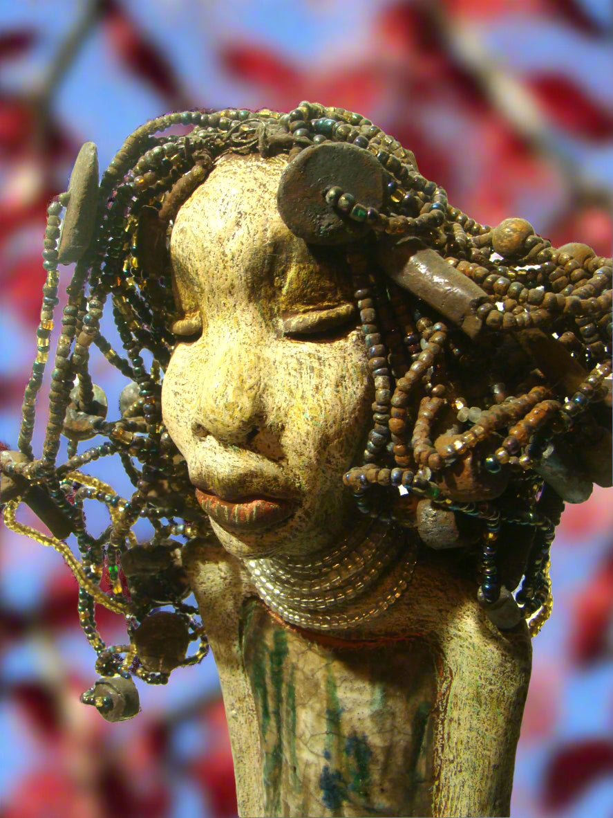 Meet Ariel, a meticulously crafted beauty. Standing at 21" x 9" x 4.5" and weighing 7lbs, she boasts a stunning beige and honey brown complexion. Her head is adorned with a variety of seed, pony, and raku beaded hair, adding to her allure. Adorned in a metallic alligator green dress with hints of shimmering copper, Ariel commands attention with her exotic gaze.