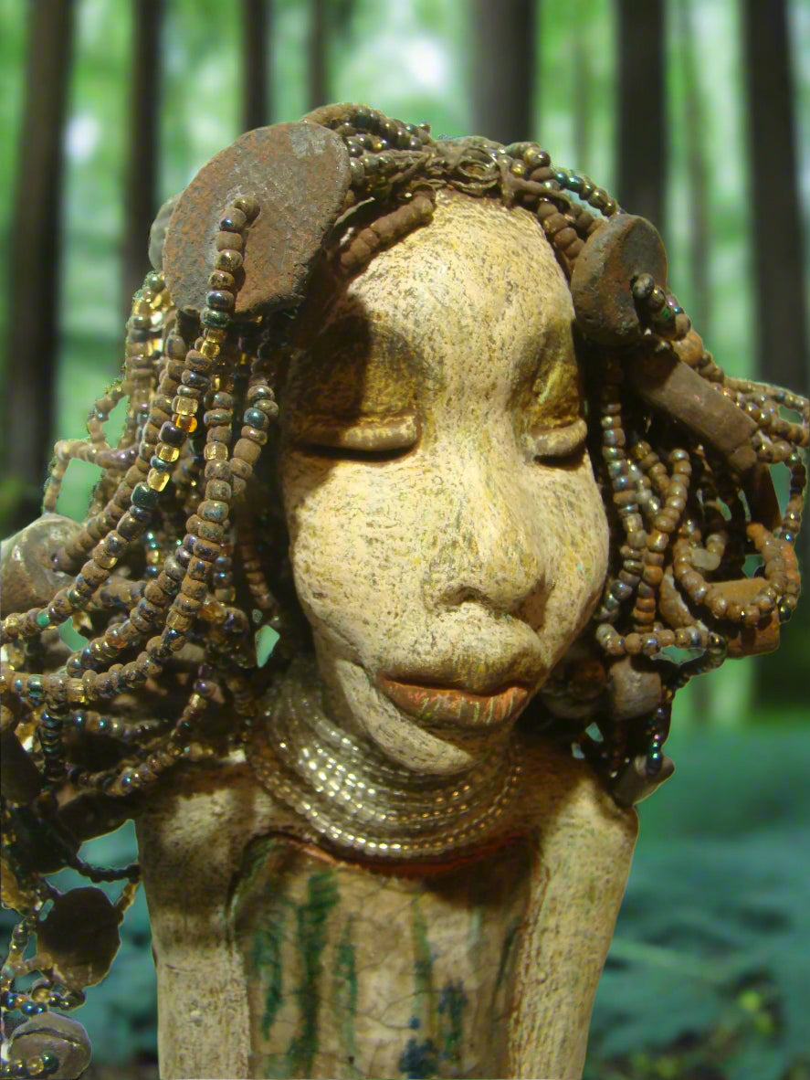Meet Ariel, a meticulously crafted beauty. Standing at 21" x 9" x 4.5" and weighing 7lbs, she boasts a stunning beige and honey brown complexion. Her head is adorned with a variety of seed, pony, and raku beaded hair, adding to her allure. Adorned in a metallic alligator green dress with hints of shimmering copper, Ariel commands attention with her exotic gaze.