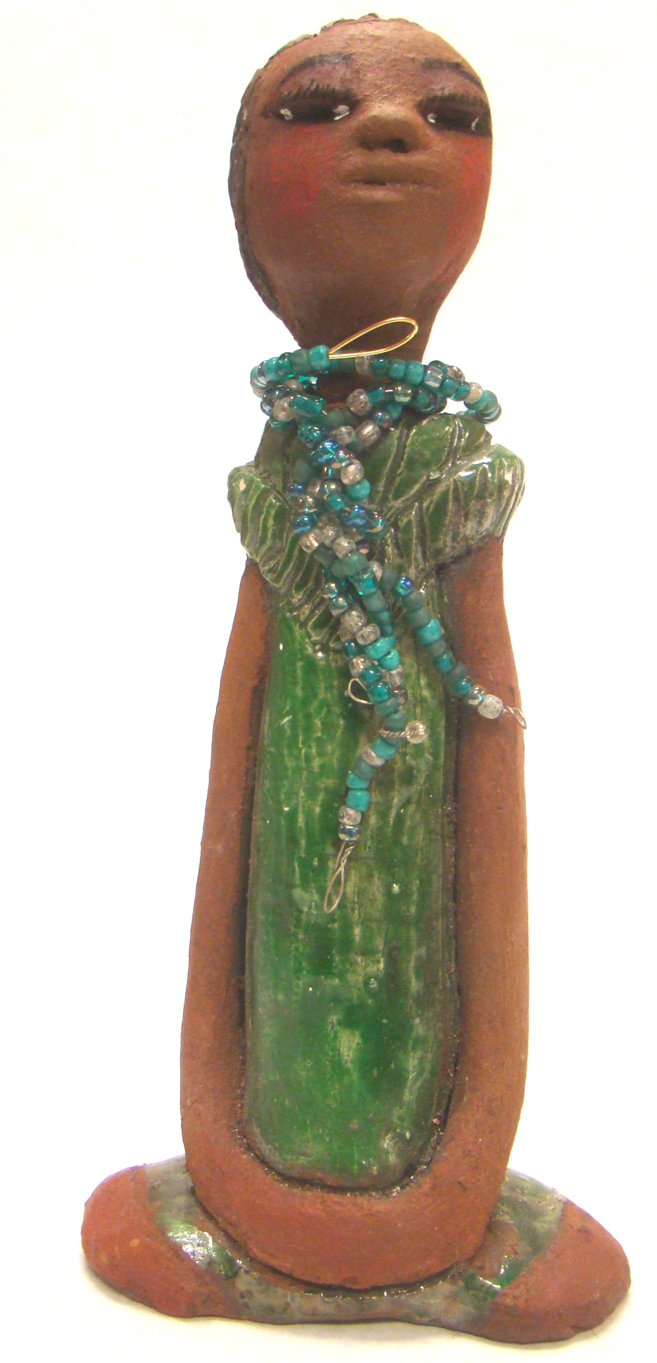 Fatou stands 9" x 4.5" x 2" and weighs 1.03 lbs. She has a lovely honey brown complexion and long loving arms. Fatou has an emerald glazed dress with a strand of multicolored beads. Her hair is raku smokey black and is etched in clay. Fatou is eye catching and will grace your surroundings.