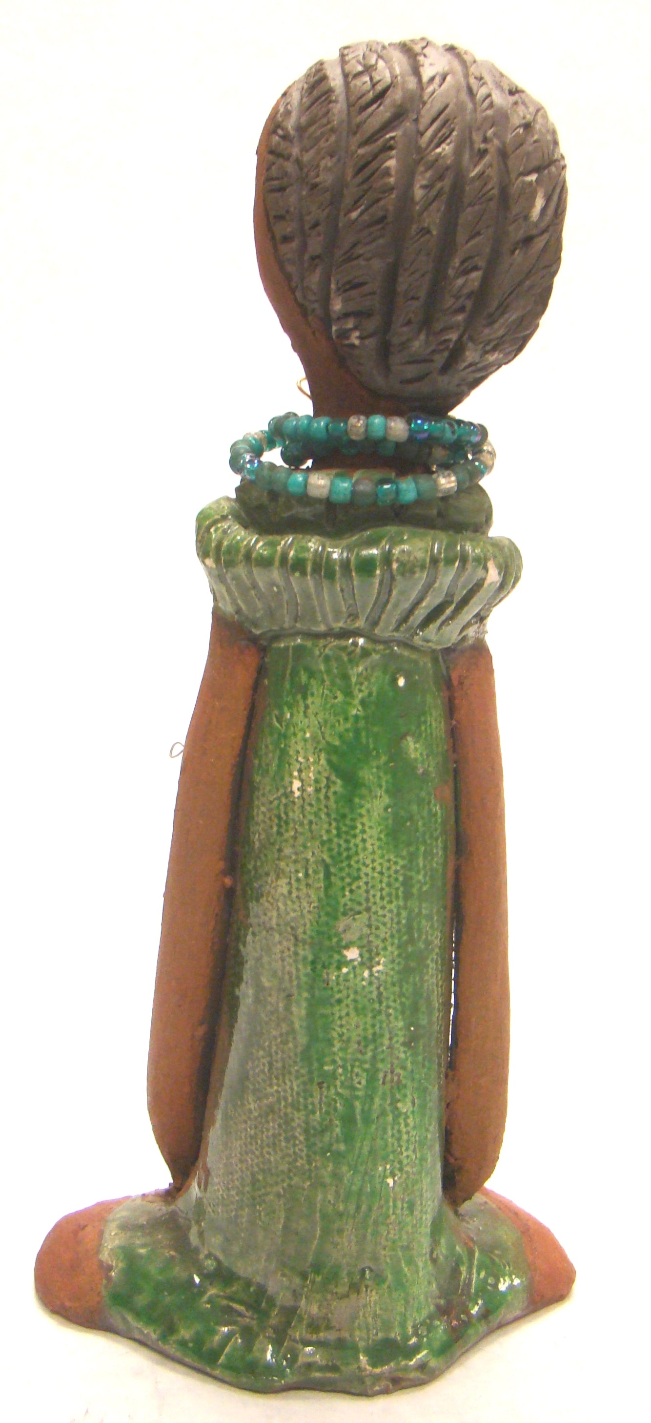 Fatou stands 9" x 4.5" x 2" and weighs 1.03 lbs. She has a lovely honey brown complexion and long loving arms. Fatou has an emerald glazed dress with a strand of multicolored beads. Her hair is raku smokey black and is etched in clay. Fatou is eye catching and will grace your surroundings.
