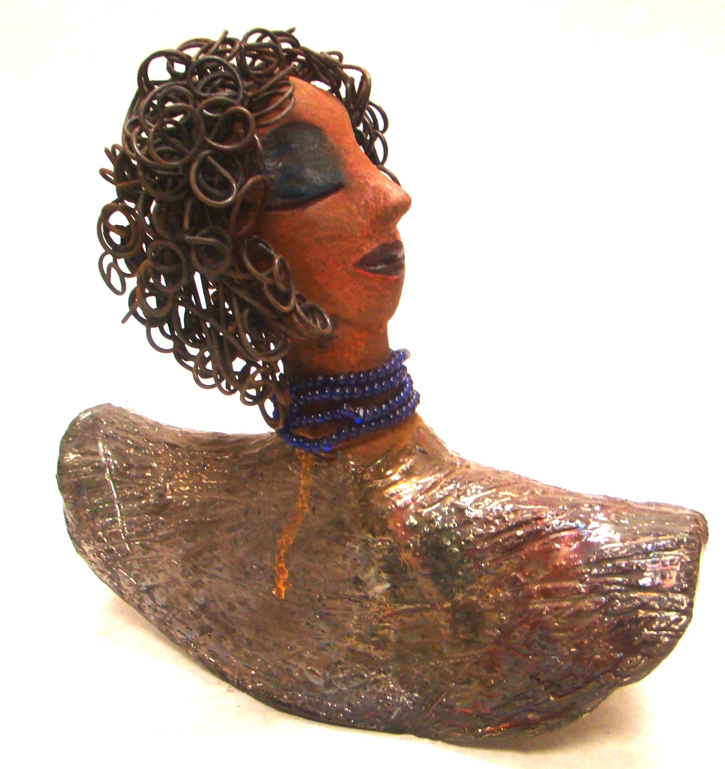 Helen stands 8" x 8" x 3" and weighs 2.06 lbs. She has a lovely honey brown complexion. Helen has a metallic copper glaze on her textured robe. Her blue eye shadow matches the blue strand of beads around her neck. Helen has over 20 feet of curly wire hair. Helen is somewhat angelic! Give Helen a prominent place in your home!