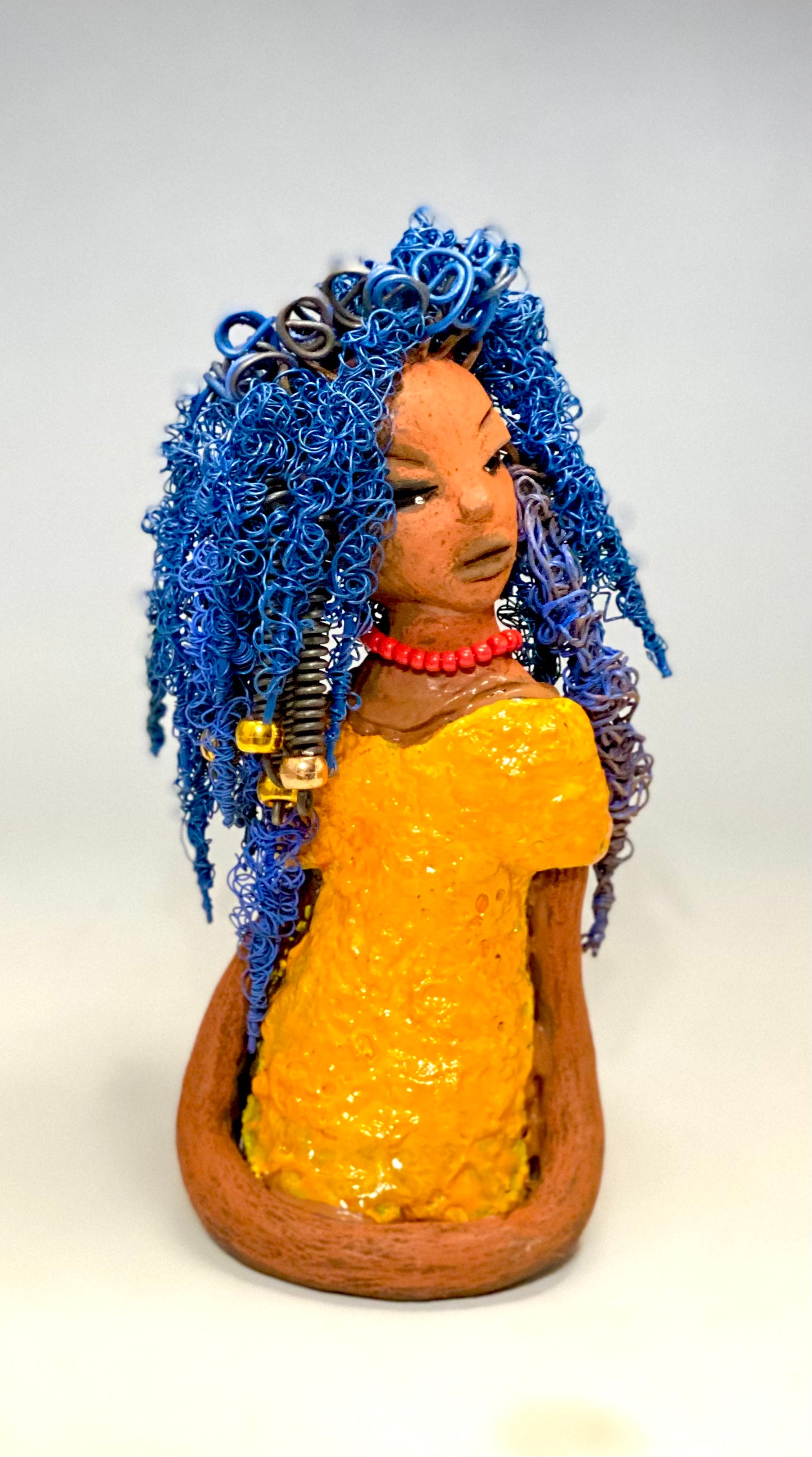 Makeba stands 8" x 5" x 5" and weighs 1.4 lbs. She has a lovely honey brown complexion with cocoa red lips. She has long twisted blue wire locs hairstyle waist down! Makeba has a sunset yellow red glazed dress. She has over 75 feet of 16 and 24 gauge blue wire for hair. It took over 5 hours just to do her hair! With eyes wide opened and a subdue look, Makeba has hope of finding a new home.