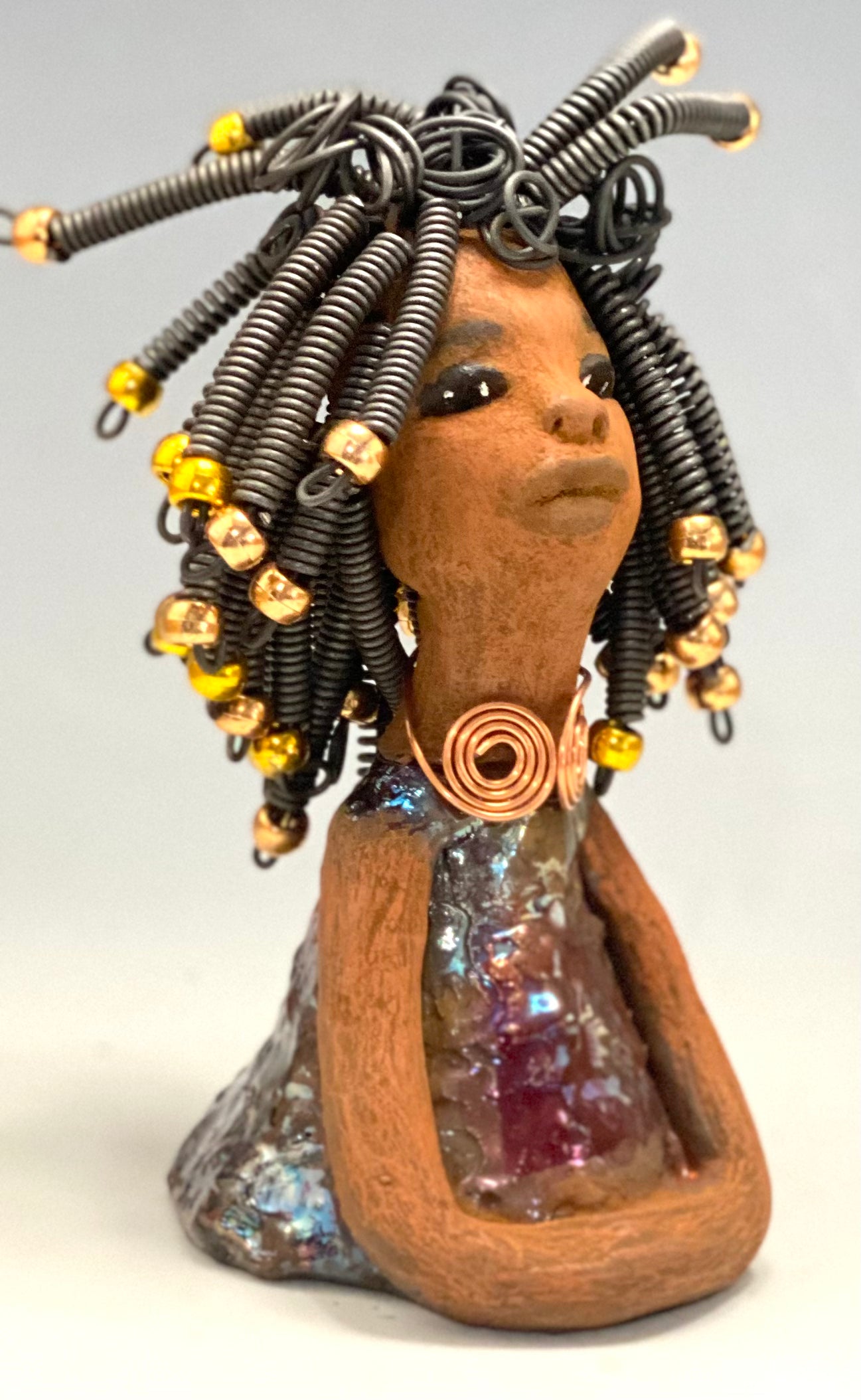 Meet Alexus Alexus stands 7.5" x 4" x 4" and weighs 1.05 lbs. She wears a lovely glossy metallic gold dress adorn by a spiral copper necklace. Alexus has over15 feet of coiled wire hair with gold beads.. Alexus appears to sit in a yoga pose. Her long arms rest at her side. Alexus is a great starter piece from the Herdew Collection!