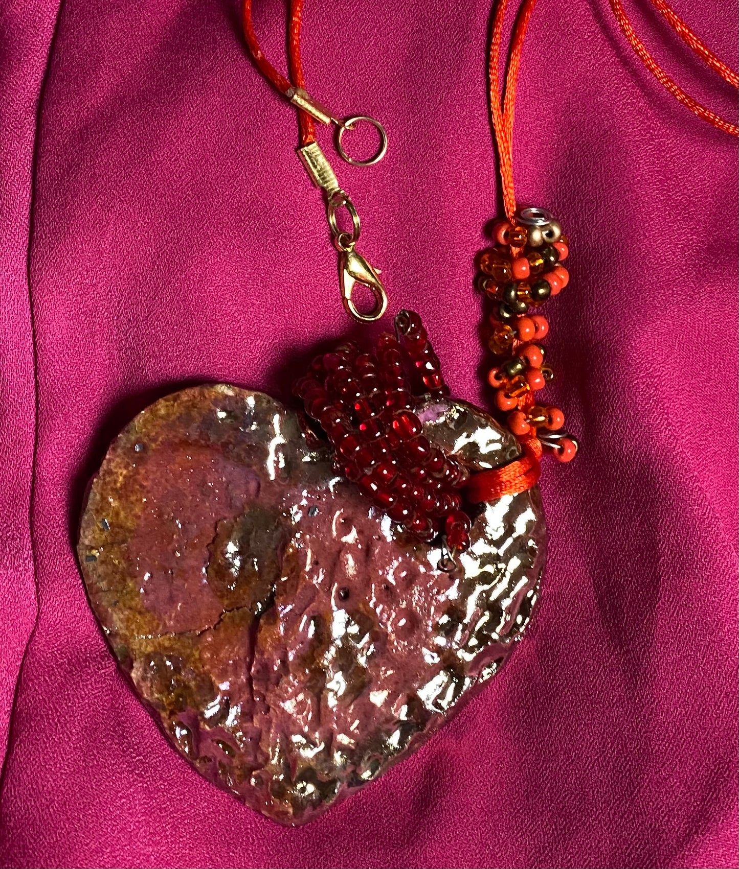 Have A Heart ! Each heart pendant is handmade with love! It is 3"x 3" and weighs approx. 3ozs. This pendant has a red violet and gold metallic raku glazes that renders a unique translucent patina. The heart has a textured pattern . Both sides are are different and equally beautiful! It holds a spiral of red violet mini beads on a spiral copper wire. This pendant has a nice 12" red suede cord!