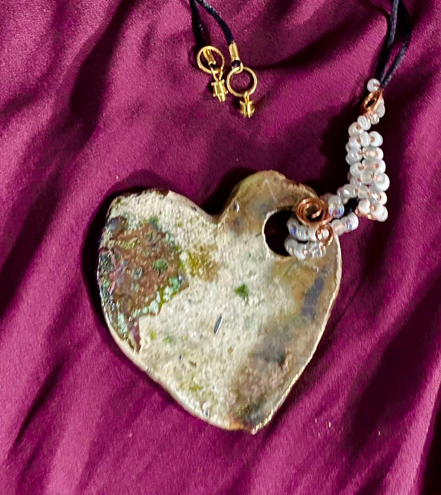 Have A Heart ! Each heart pendant is handmade with love! It is 3"x 3" and weighs approx. 3ozs. This pendant has a toasty white copper metallic raku glazes that renders a unique translucent  patina. The heart has a textured pattern . Both sides are  are different and equally beautiful! It holds a spiral of white  mini beads on a spiral copper wire. This pendant has a nice 12"  black rattail cord!