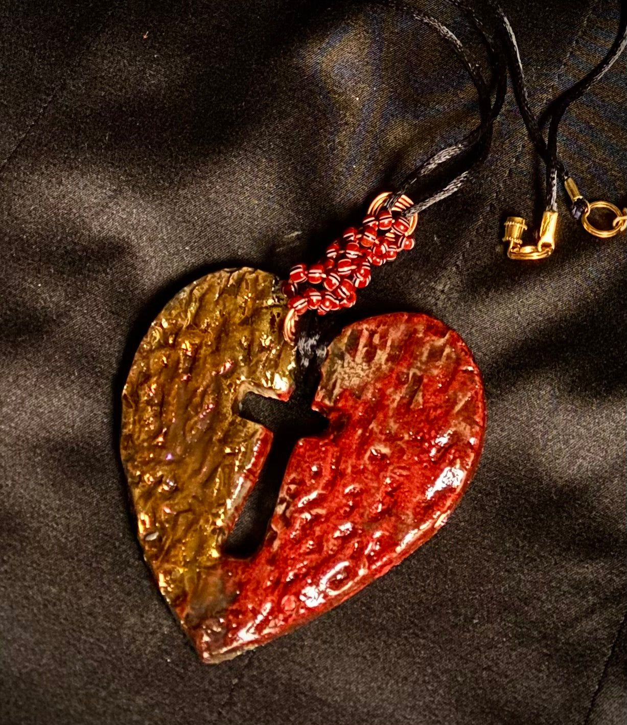 Have A Heart ! Each heart pendant is handmade with love! It is 3"x 3" and weighs approx. 3ozs. This pendant has a red and gold metallic raku glazes that renders a unique translucent patina. The heart is textured and has a cut out cross in the center. It holds a spiral of red and white mini beads on a spiral copper wire. This pendant has a nice 12" black suede cord!