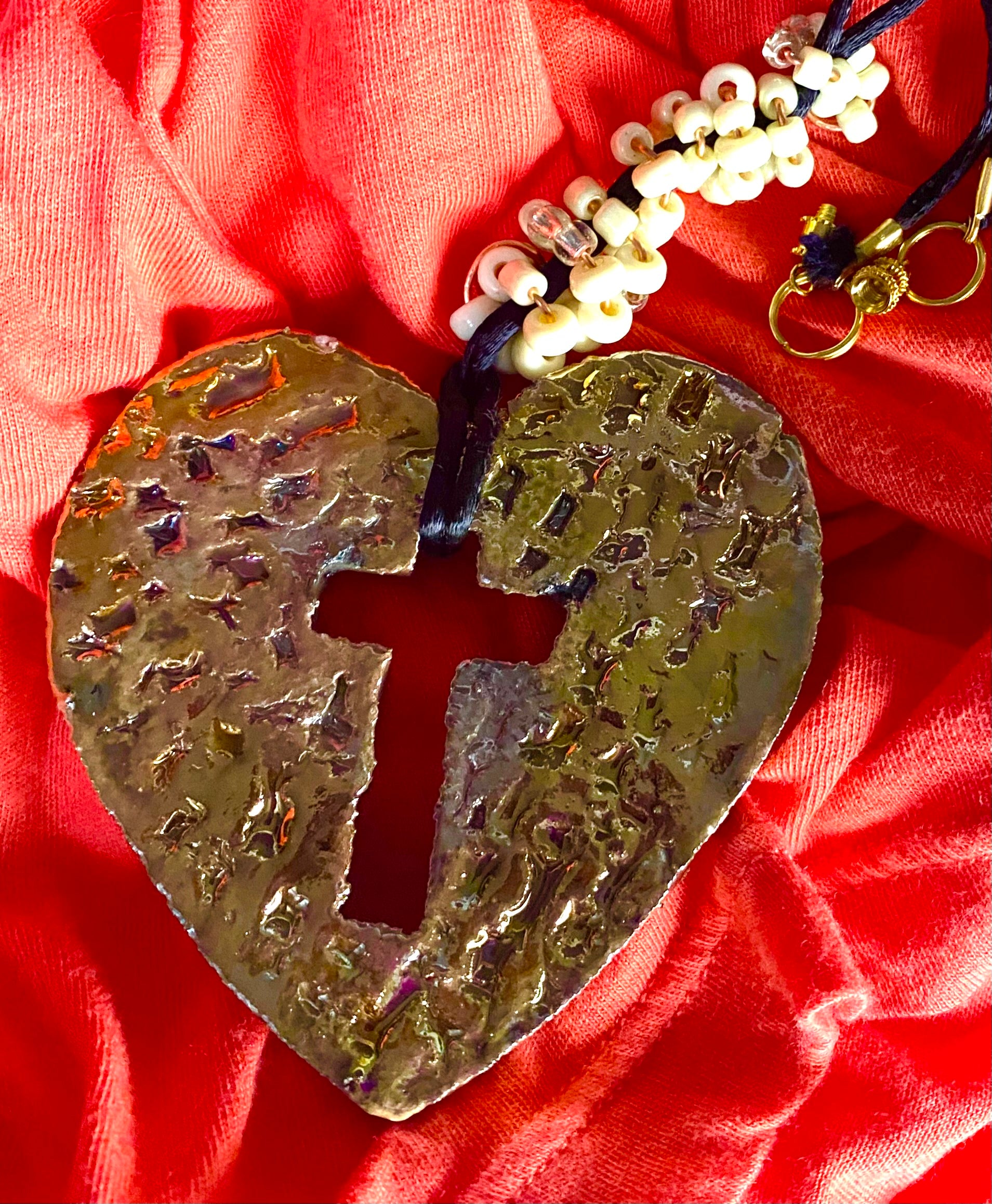 Have A Heart ! Each heart pendant is handmade with love! It is 3"x 3" and weighs approx. 3ozs. This pendant has an off white and gold metallic raku glazes that renders a unique translucent  patina. The heart  has a textured  pattern with a cut out cross in the center.. It holds a spiral of off white mini beads on a spiral copper wire. This pendant has a nice 12" black suede cord!