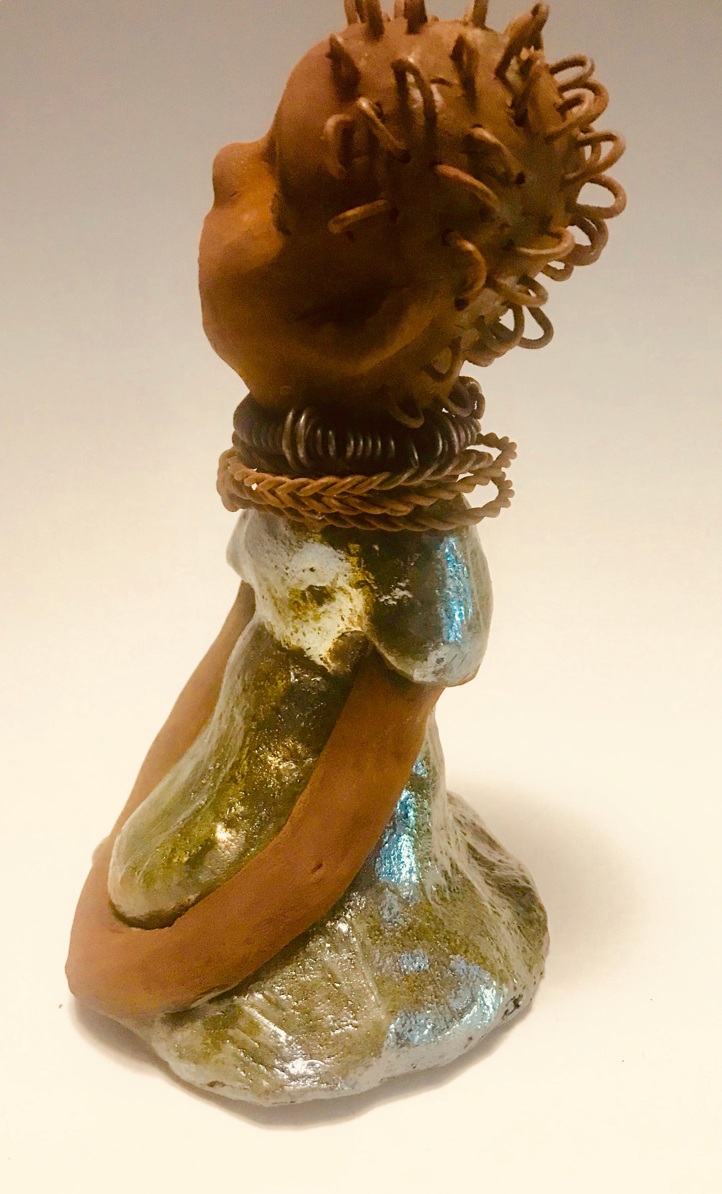 Nura stands 7.5" x 5" x 5" and weighs 1.06 lbs. She has a lovely honey brown complexion with reddish brown lips. She has a wire braided hairstyle. Nura has a colorful metallic green antique copper glazed dress. She wears spiral wire necklaces With her eyes wide opened, Nura has hopes of finding a new home.