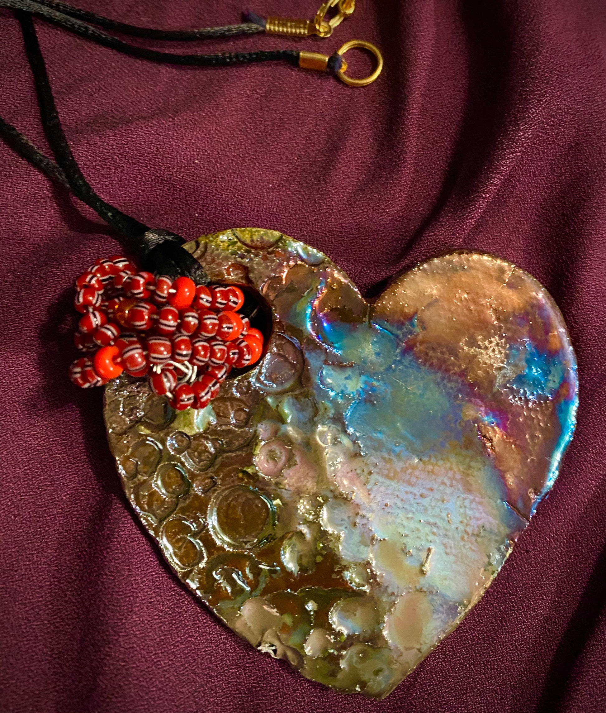 Have A Heart ! Each heart pendant is handmade with love! It is 3"x 3" and weighs approx. 3ozs. This pendant has a colorful copper metallic raku glazes that renders a unique translucent patina. The heart has a textured pattern . Both sides are  are different and equally beautiful! It holds a spiral of blue mini beads on a spiral copper wire. This pendant has a nice 12" black rattail  cord!
