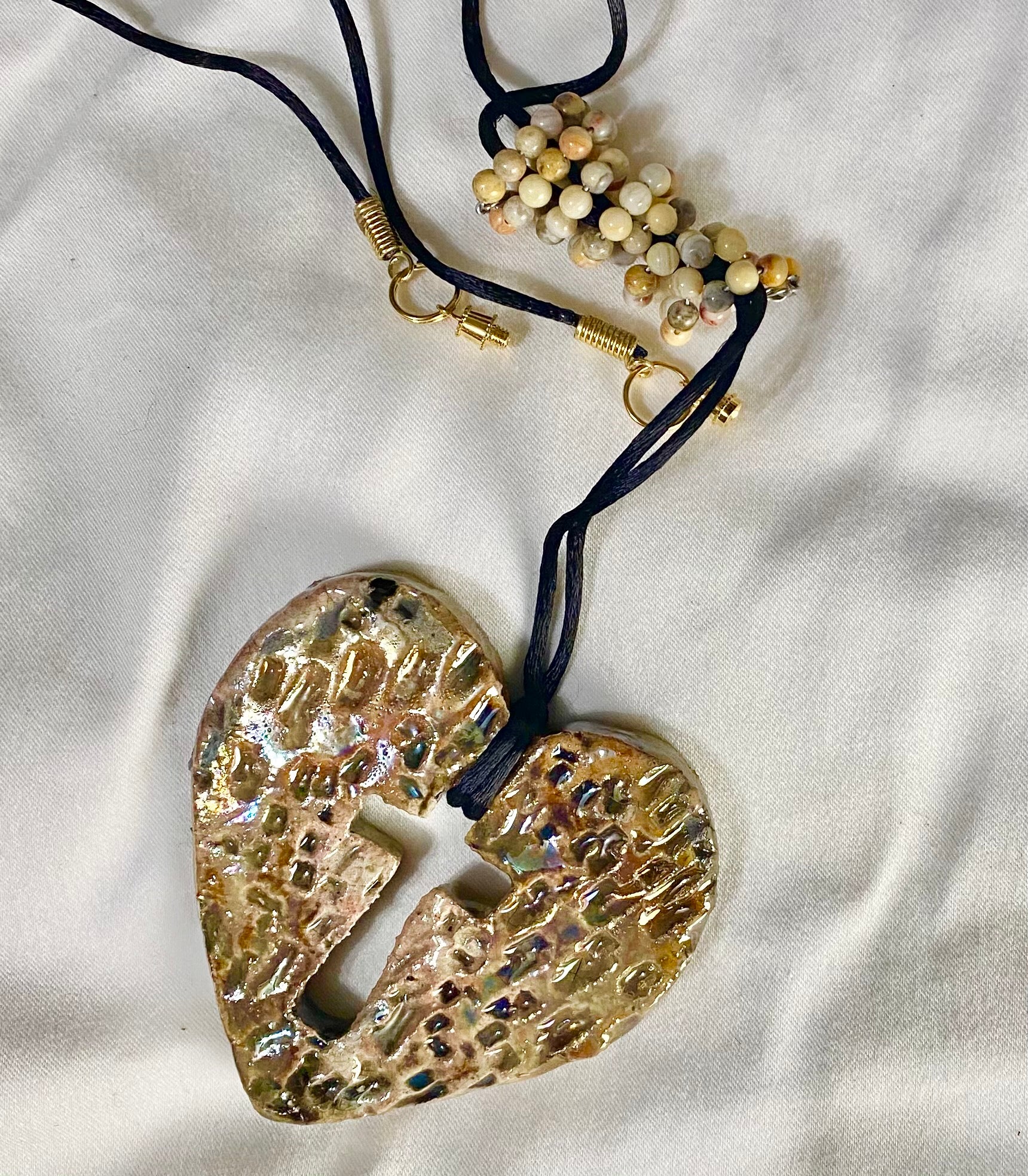 Have A Heart ! Each heart pendant is handmade with love! It is 3"x 3" and weighs approx. 3ozs. This pendant has a white and gold metallic raku glazes that renders a unique translucent  patina. The heart has a textured with cut out cross pattern . It holds a spiral of multicolored mini beads on a spiral copper wire. This pendant has a nice 12" black suede cord!