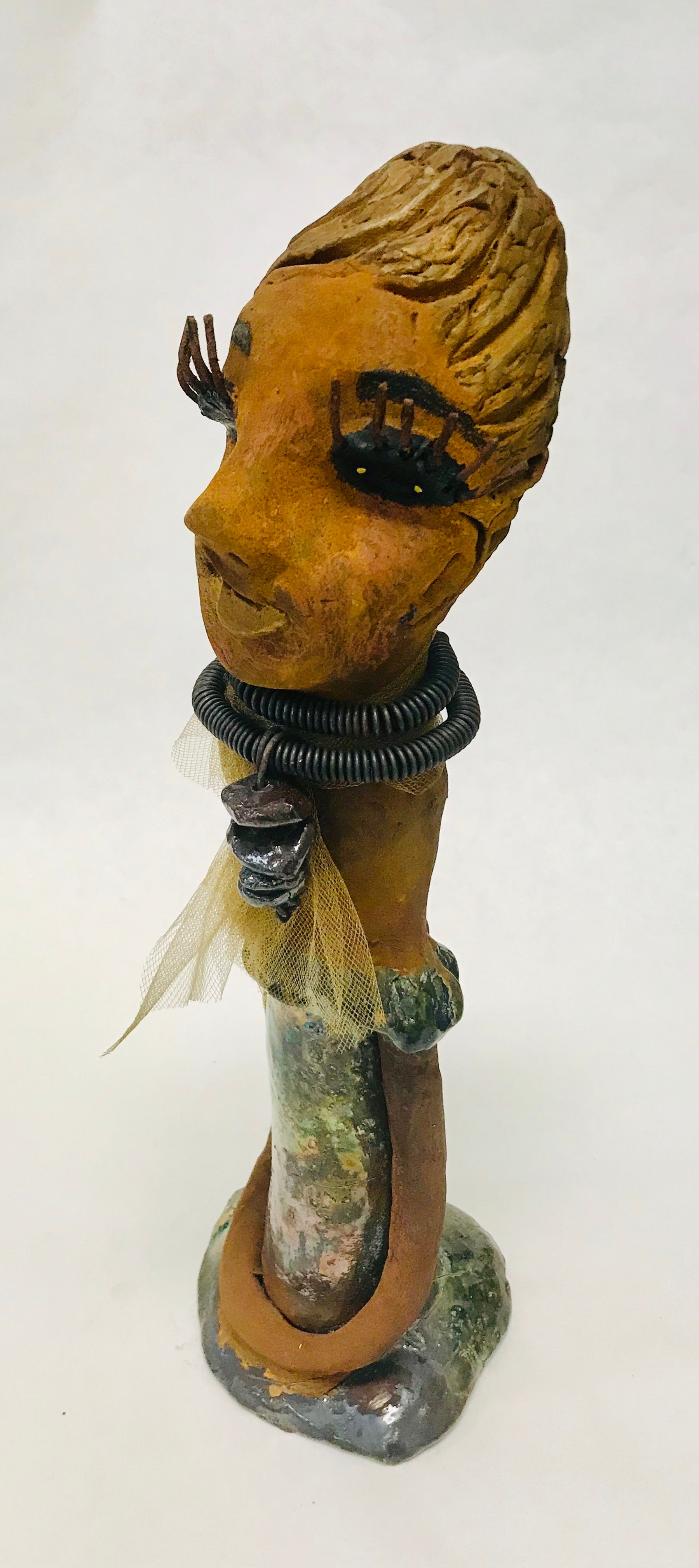 Trinity stands 14" x 4" x 4" and weighs 2.7 lbs. She has a lovely honey brown complexion with  reddish brown lips. She has a braided hairstyle.  Trinity has a colorful metallic green antique copper glazed dress. She wears a spiral wire necklaces with raku beads underneath an antique gold tulle.. With long lashes and eyes wide opened, Trinity has hopes of finding a new home.
