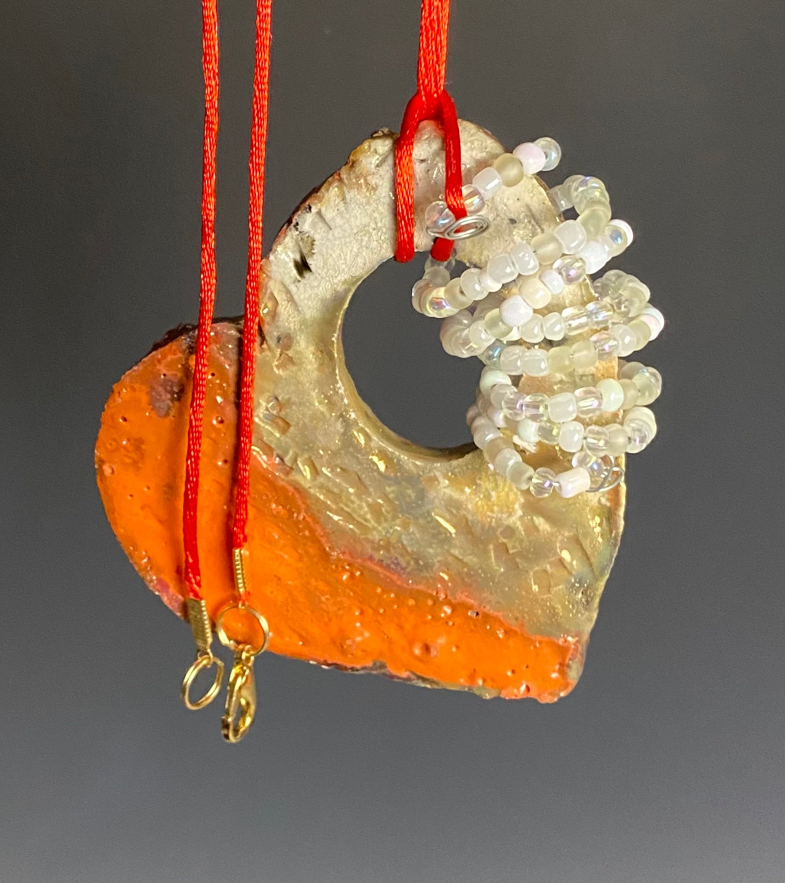 Have A Heart ! Each heart pendant is handmade with love! It is 3"x 3"and weighs approx. 3ozs. This pendant has a red violet and gold metallic raku glazes that renders a unique translucent  patina. The heart has a textured pattern . Both sides are  are different and equally beautiful! It holds a spiral of white and clear mini beads on a spiral copper wire. This pendant has a nice 12" red suede cord!