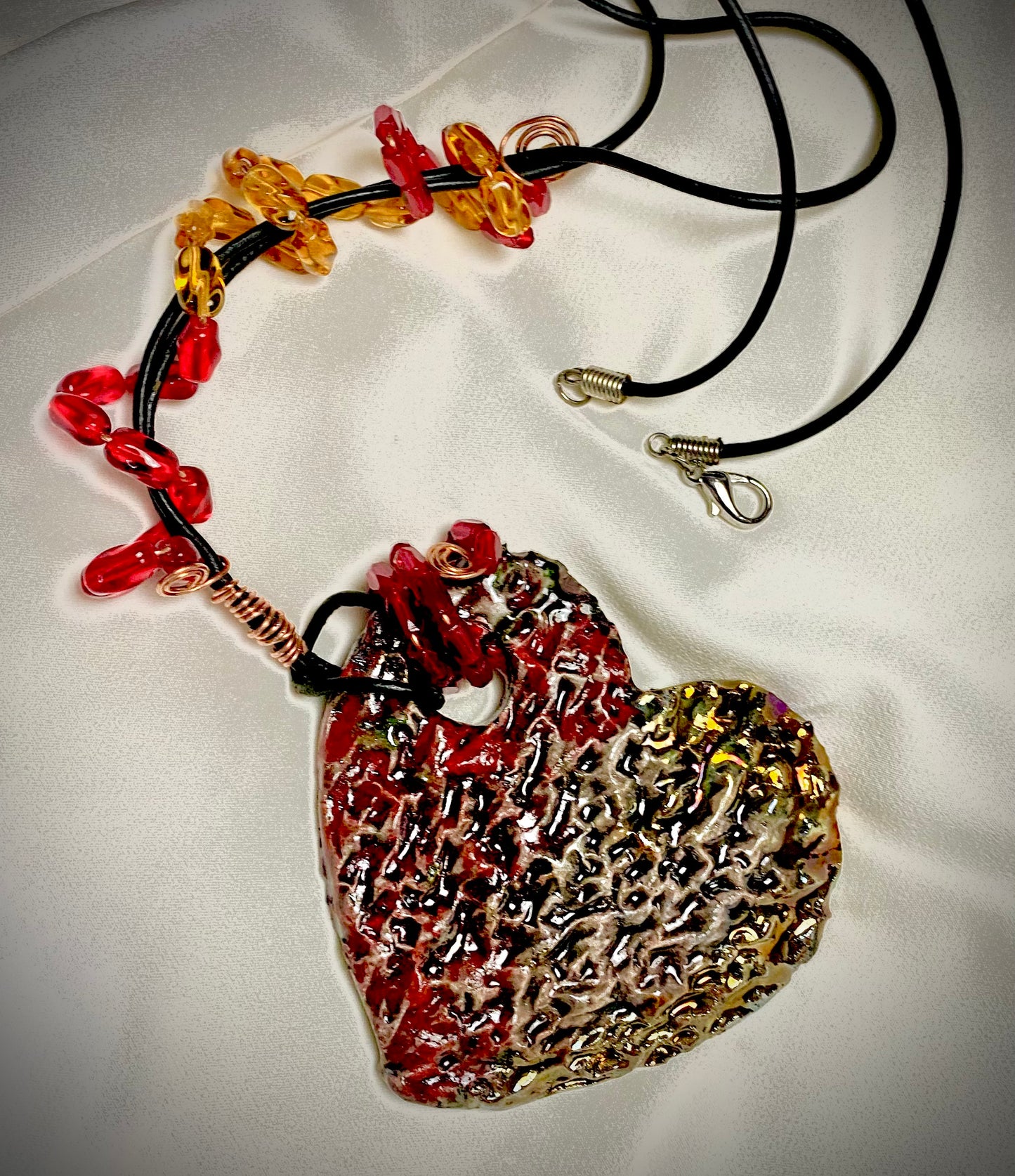 Have A Heart ! Each heart pendant is handmade with love! It is 3"x 3" and weighs approx. 3ozs. This pendant has a red and gold metallic raku glazes that renders a unique translucent patina. The heart has a textured pattern . It holds a spiral of amber and red mini beads on a spiral copper wire. This pendant has a nice 12" black suede cord!