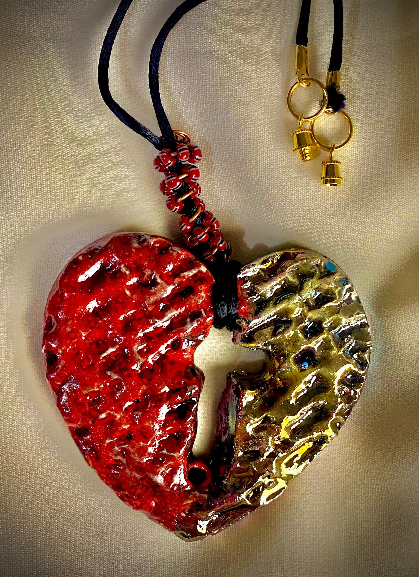 Have A Heart ! Each heart pendant is handmade with love! It is 3"x 3" and weighs approx. 3ozs. This pendant has a ruby red and gold metallic raku glazes that renders a unique translucent patina. The heart has a textured pattern with a cut out cross in the center.. It holds a spiral of ruby red mini beads on a spiral copper wire. This pendant has a nice 12" black suede cord!