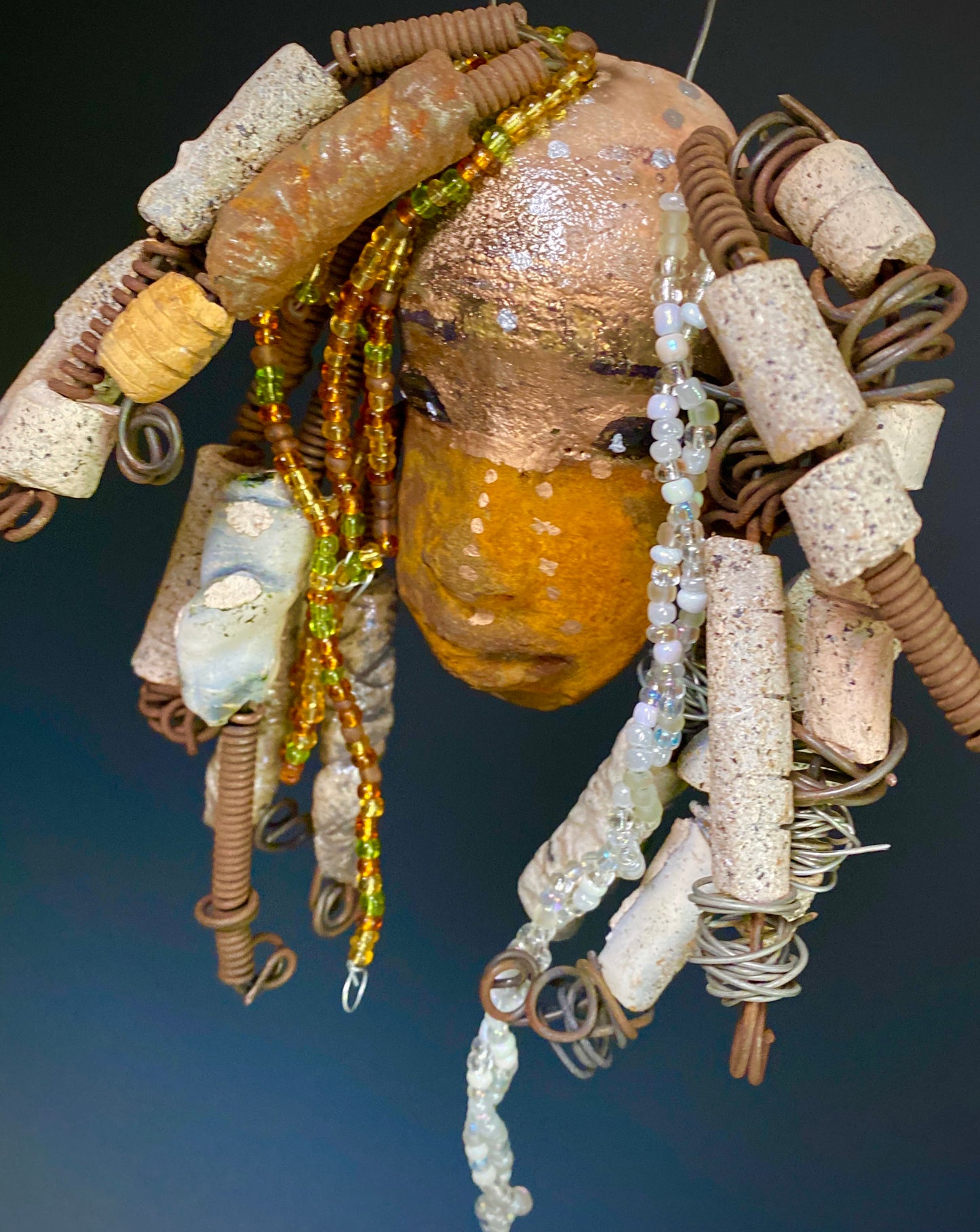 I started making art soon after seeing authentic African artwork at the Smithsonian Museum of African Art. I was in total awe. Ryanna was inspired by my visit there. Ryanna is 8”x 6” and weighs 13 ozs. She has a two tone earthy honey and metallic gold complexion. Ryanna has over 20 raku beads and over a 100 mini colored and white beads spiral coils of hair. She more than 10 feet of 16 gauge wire hair