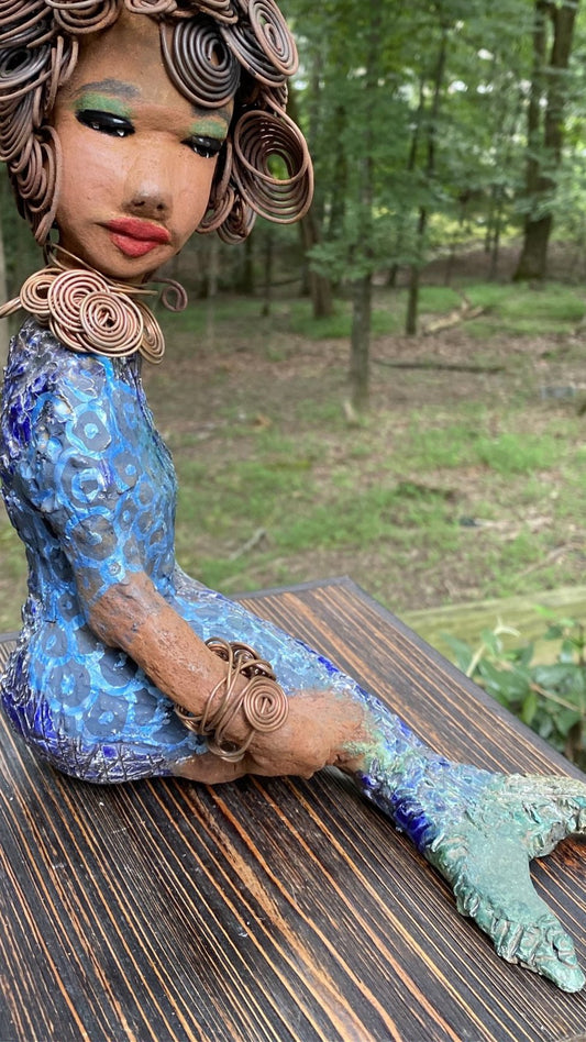 Meet Shelia E.! She is such a Lady I mean Mermaid!    Shelia stands 12" x 10" x 4" and weighs 3.13 lbs. Shelia has a two tone honey brown complexion. She has over 15 feet of spiral wire hair which took over two hours to style. Shelia wears a textured sky blue swimsuit Her layered spiral copper necklace hangs above her long loving arm. Shelia is such a ladylike Mermaid. She sits tall and proud. Compare her to Harmony the mermaid. Give Shelia or Harmony a special place to sit in your home!