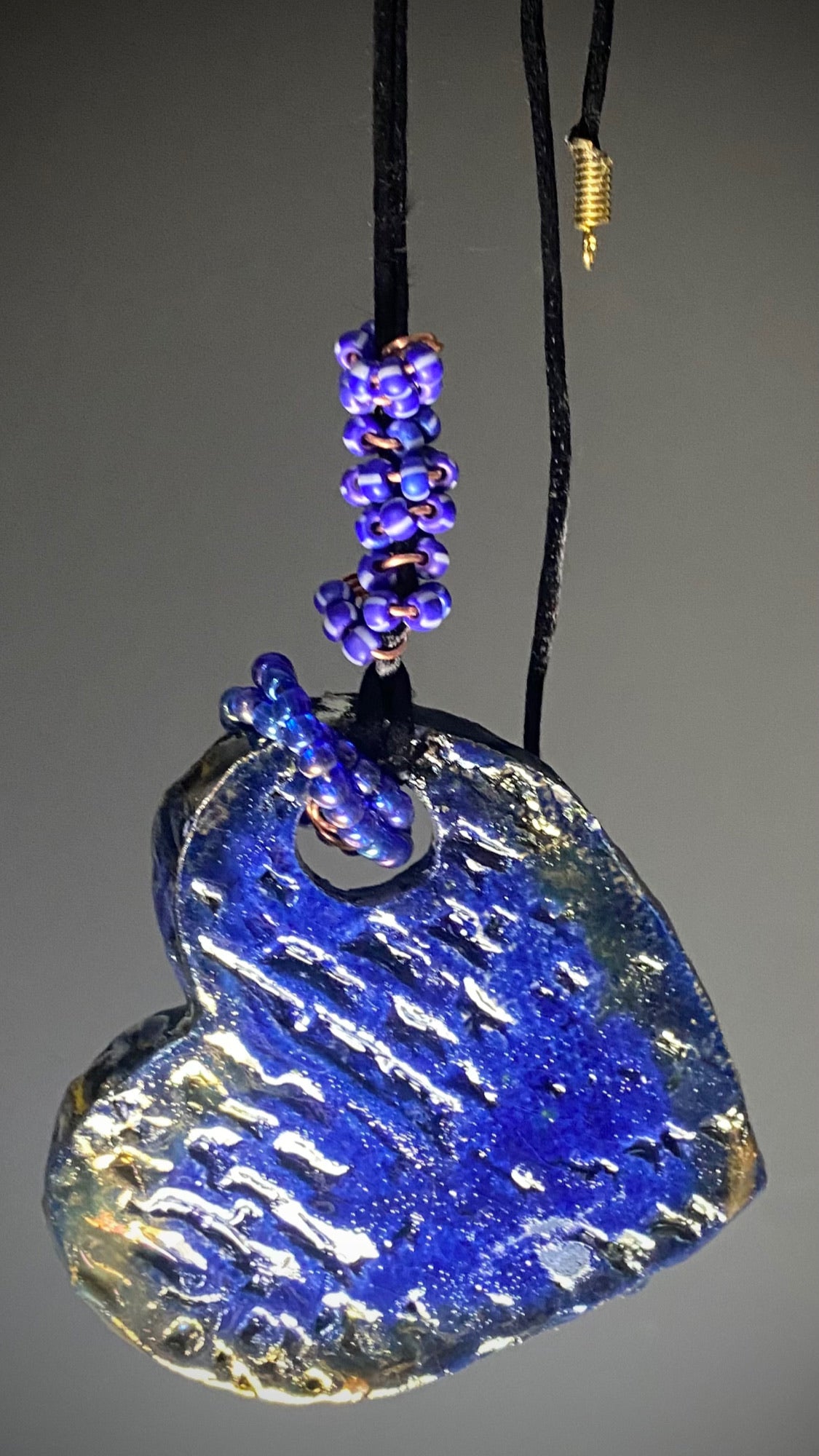Have A Heart! Each heart pendant is handmade with love! It is 3"x 3"and weighs approx. 3ozs. This pendant has a blue and gold raku glazes that renders a unique translucent patina. The heart has a textured pattern! Both sides are are different and equally beautiful! There is a spiral of blue mini beads on copper in the center. This pendant has a nice 12" black adjustable rattail cord!