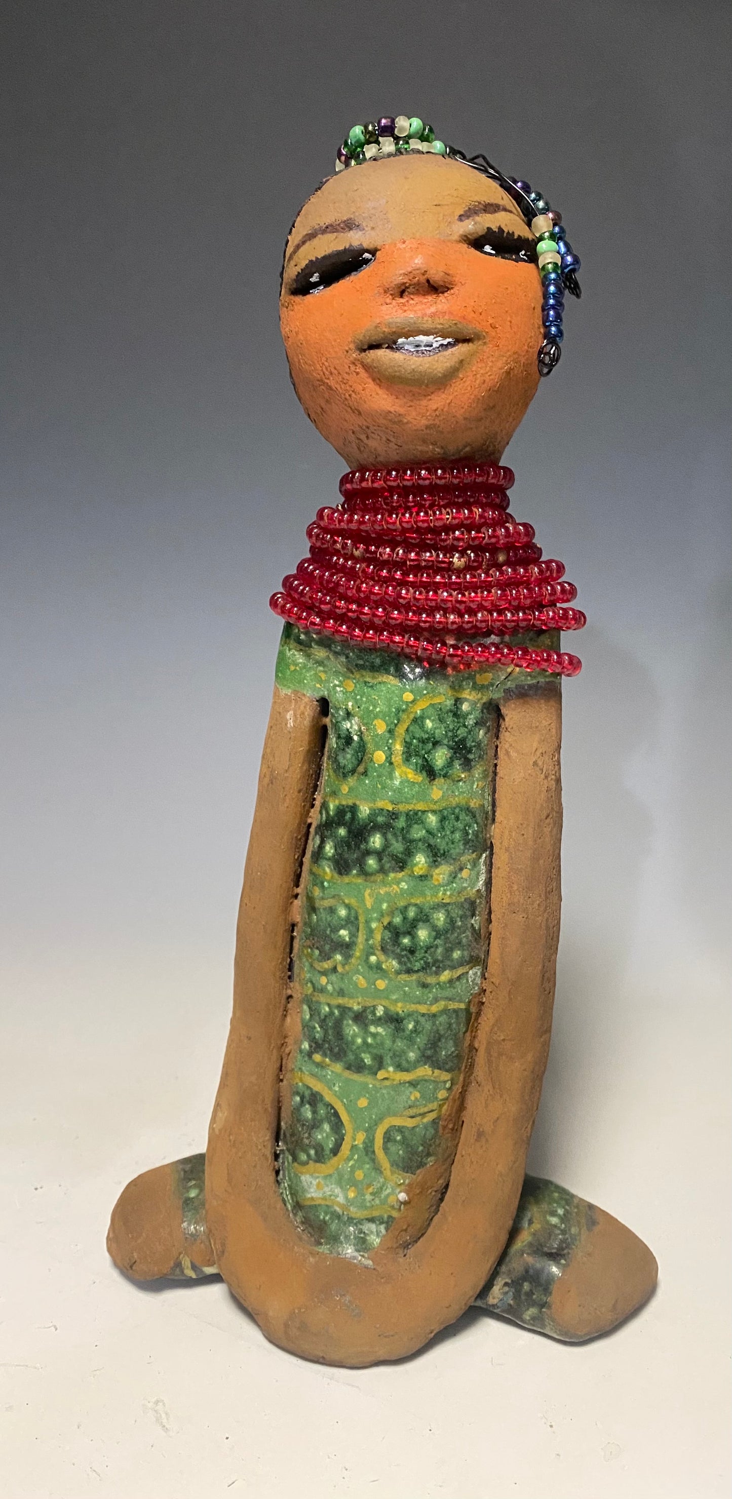 Meet Julia! Julia stands 10" x 6" x 5" and weighs 1.10 lbs. She has a lovely two tone honey brown complexion. Julia black etched hair has two beaded braids! Julia has a metallic antique copper green glazed dress. With her eyes opened and her long arms at her side, she has something to say! " I am just waiting on you to invite me into your home!" Julia will place a smile on your face and spark interesting conversation!