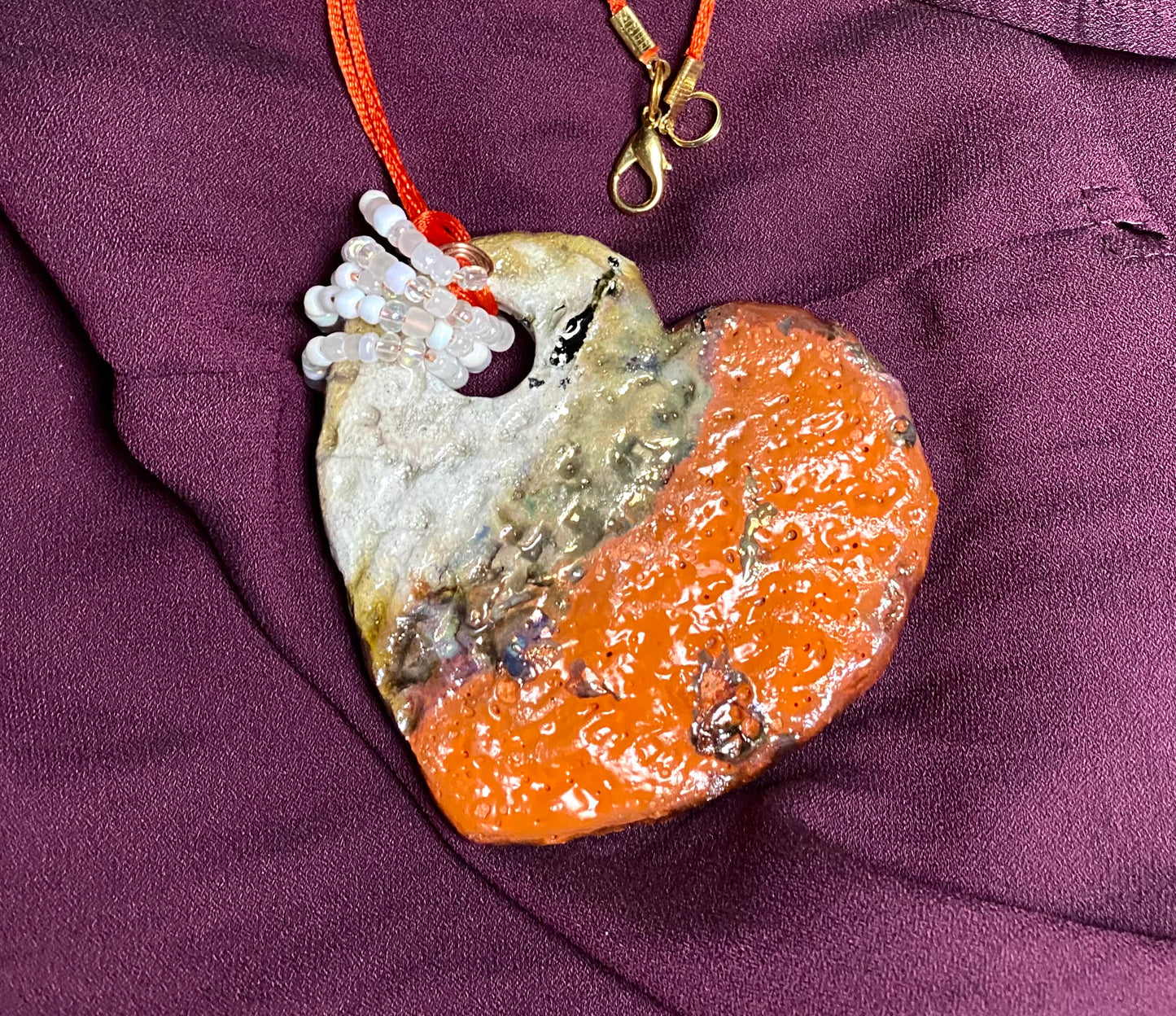 Have A Heart ! Each heart pendant is handmade with love! It is 3"x 3"and weighs approx. 3ozs. This pendant has a red violet and gold metallic raku glazes that renders a unique translucent patina. The heart has a textured pattern . Both sides are are different and equally beautiful! It holds a spiral of white and clear mini beads on a spiral copper wire. This pendant has a nice 12" red suede cord!