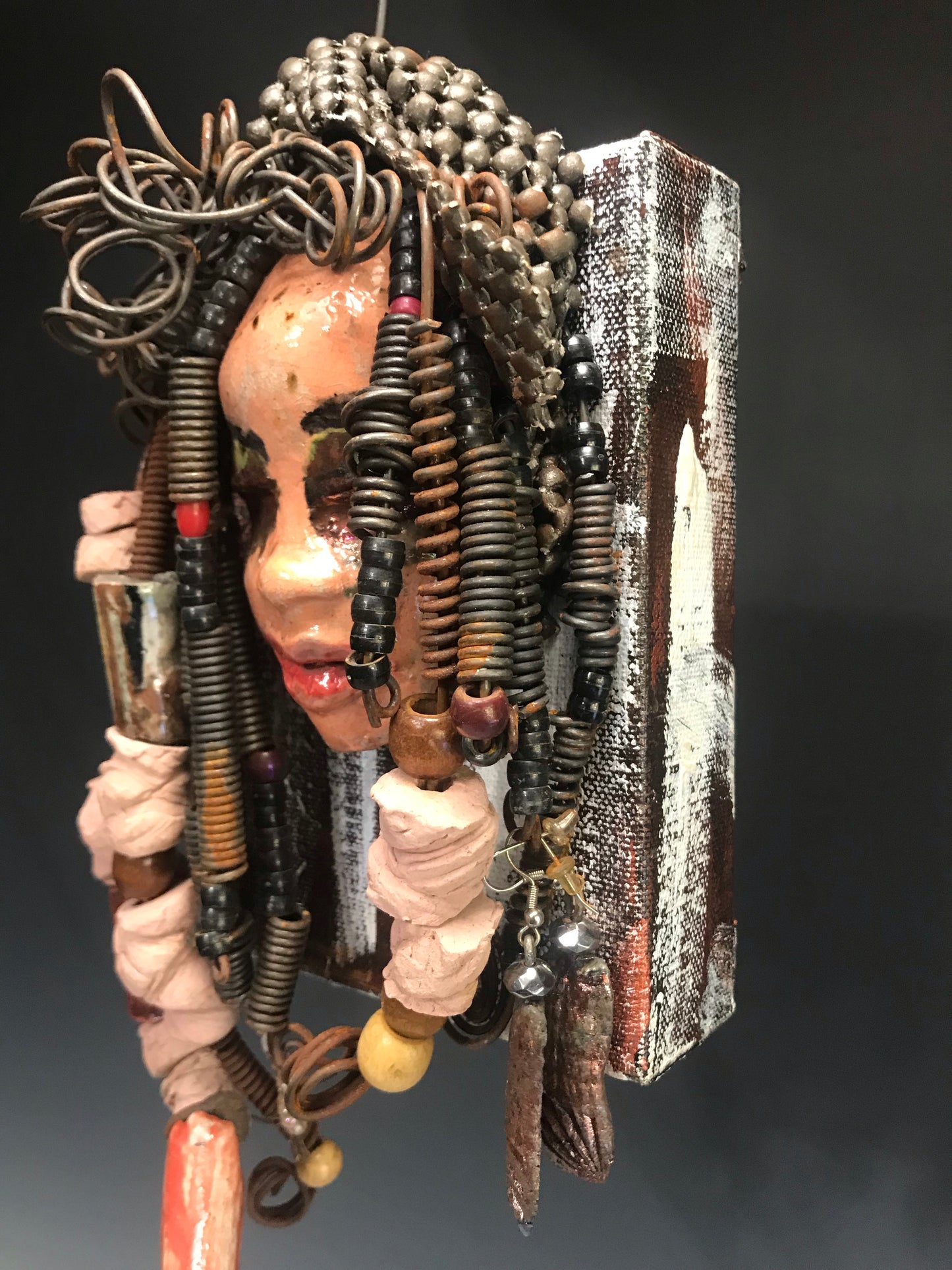 Kamara is uniquely mounted on a painted 6"x 4"x 2" canvas. It weighs 1.6lbs. Her face is formed with hand coiled wire, raku beads, textured brown cloth, and multi color raku beads. Kamara's face beams with pale pink crackle glaze and ruby red lips. Kamara is ready to be hung in a special place!