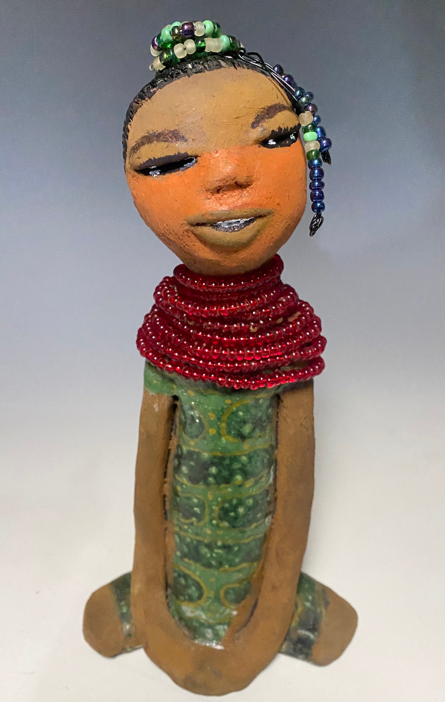 Meet Julia! Julia stands 10" x 6" x 5" and weighs 1.10 lbs. She has a lovely two tone honey brown complexion. Julia black etched hair has two beaded braids! Julia has a metallic antique copper green glazed dress. With her eyes opened and her long arms at her side, she has something to say! " I am just waiting on you to invite me into your home!" Julia will place a smile on your face and spark interesting conversation!