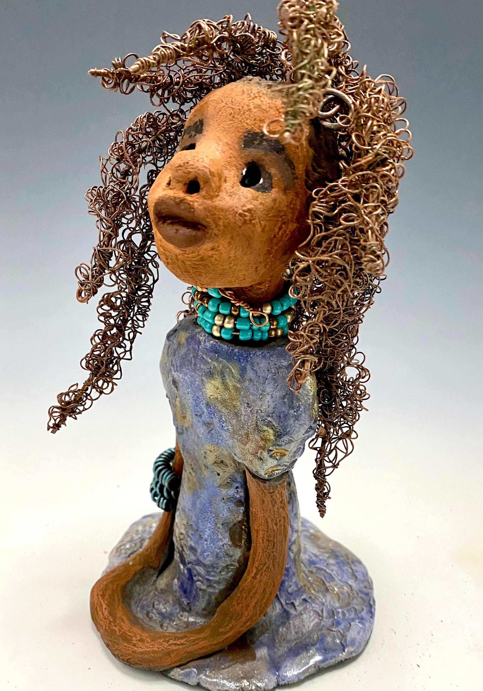 Meet Janae'! She has grown a head full of Hair! Janae' stands 8" x 5" x 4" and weighs 1.03 lbs. She has a lovely honey brown complexion with lovely reddish brown lips. Janae' wears a clay braided hairstyle. Janae' has a colorful metallic blue and gold glazed dress. She wears a blue and antique copper  beaded necklace. With eyes wide opened, Janae' has hopes of finding a new home.
