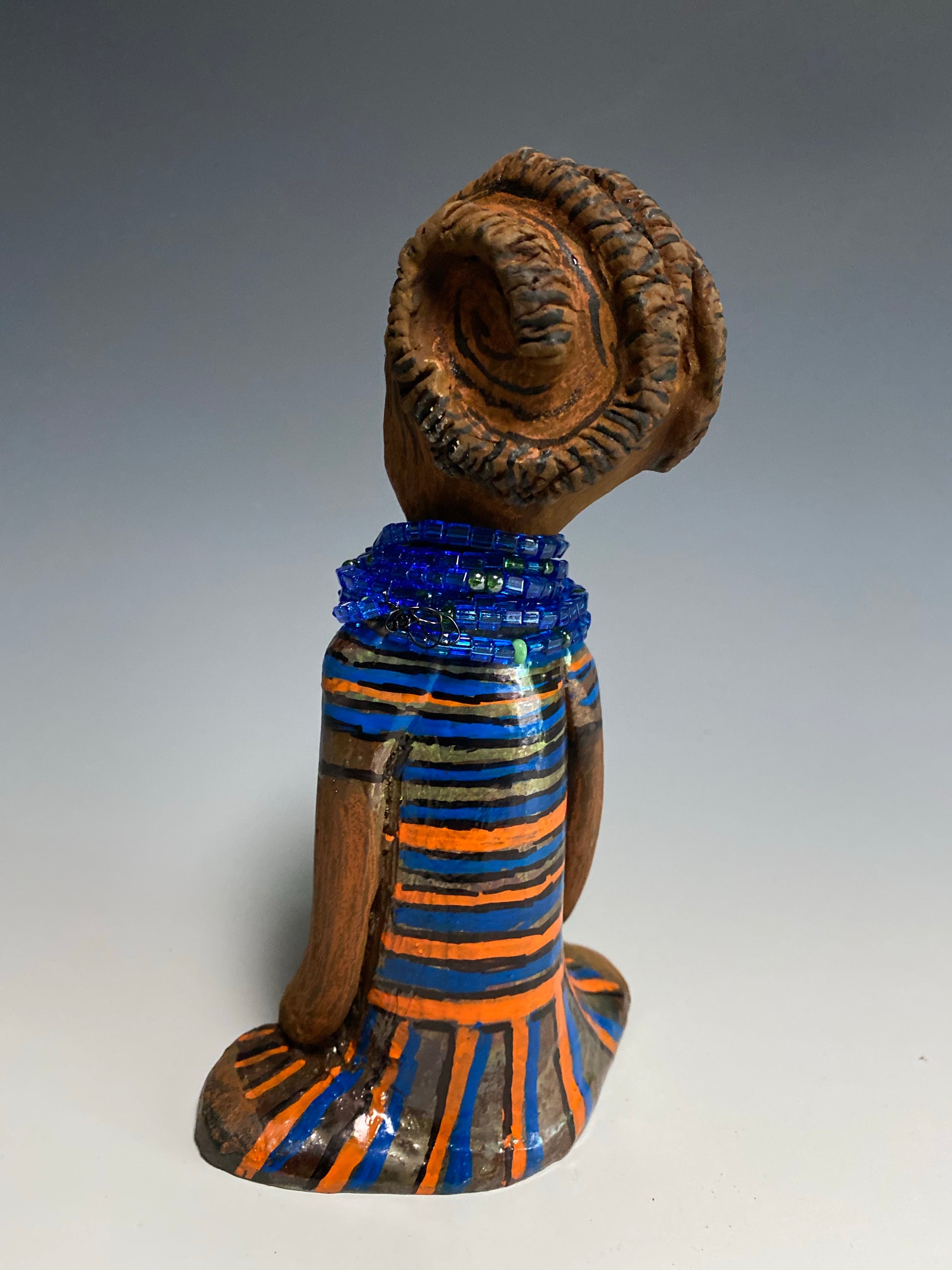 Meet Meet Harmony! Harmony stands 8' x 5"x 2" and weighs 1.7 lb. She has a nice honey brown complexion. Harmony  has stylized clay hair.  Her long trademark arms rest at her side. Harmony's dress is  colorful with  geometric flare.. She accents with a aqua blue beaded necklace. Harmony is priced right to be accepted into  your home!
