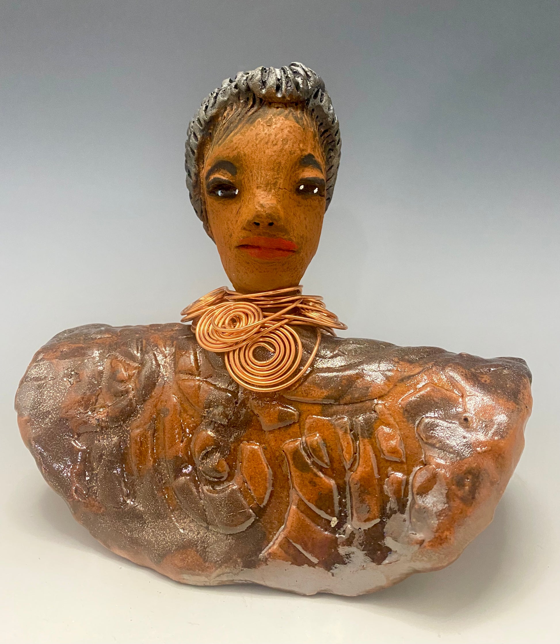 Meet Penny! Penny stands 8" x  8" x 3" and weighs 2.06 lbs. She has a lovely honey brown complexion. Penny has a metallic copper penny glaze on her textured robe. Her black eye shadow matches the black strands of baby hair around her edges. Penny's necklace has over 8 feetof spiral copper wire hair. Helen is somewhat angelic! Give Penny a porminent place in your home!