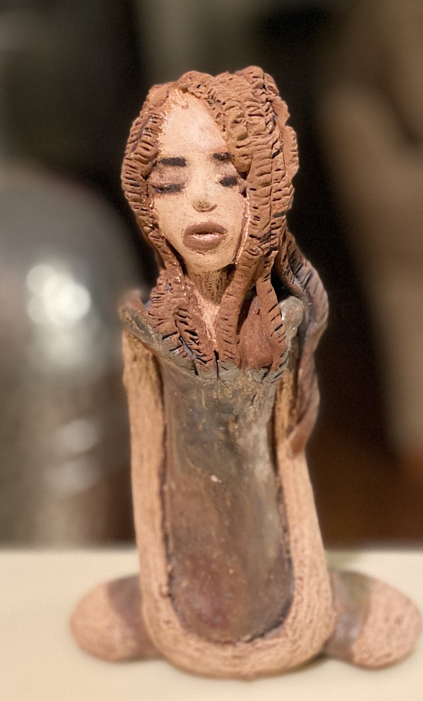 Amani stands 8" x 5" x 2.5" and weighs 1.03 lbs. She has a lovely beige brown complexion with long etched braided clay hair. Amani long loving arms rest beside her copper green dress. Amani is a sophisticated lady that will grace your home.