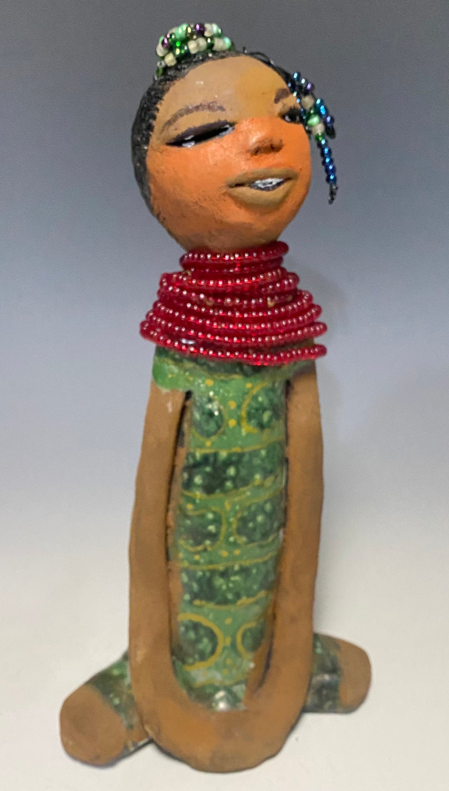 Meet Julia! Julia stands 10" x 6" x 5" and weighs 1.10 lbs. She has a lovely two tone honey brown complexion. Julia black etched hair has two beaded braids! Julia has a metallic antique copper green glazed dress. With her eyes opened and her long arms at her side, she has something to say! " I am just waiting on you to invite me into your home!" Julia will place a smile on your face and spark interesting conversation!