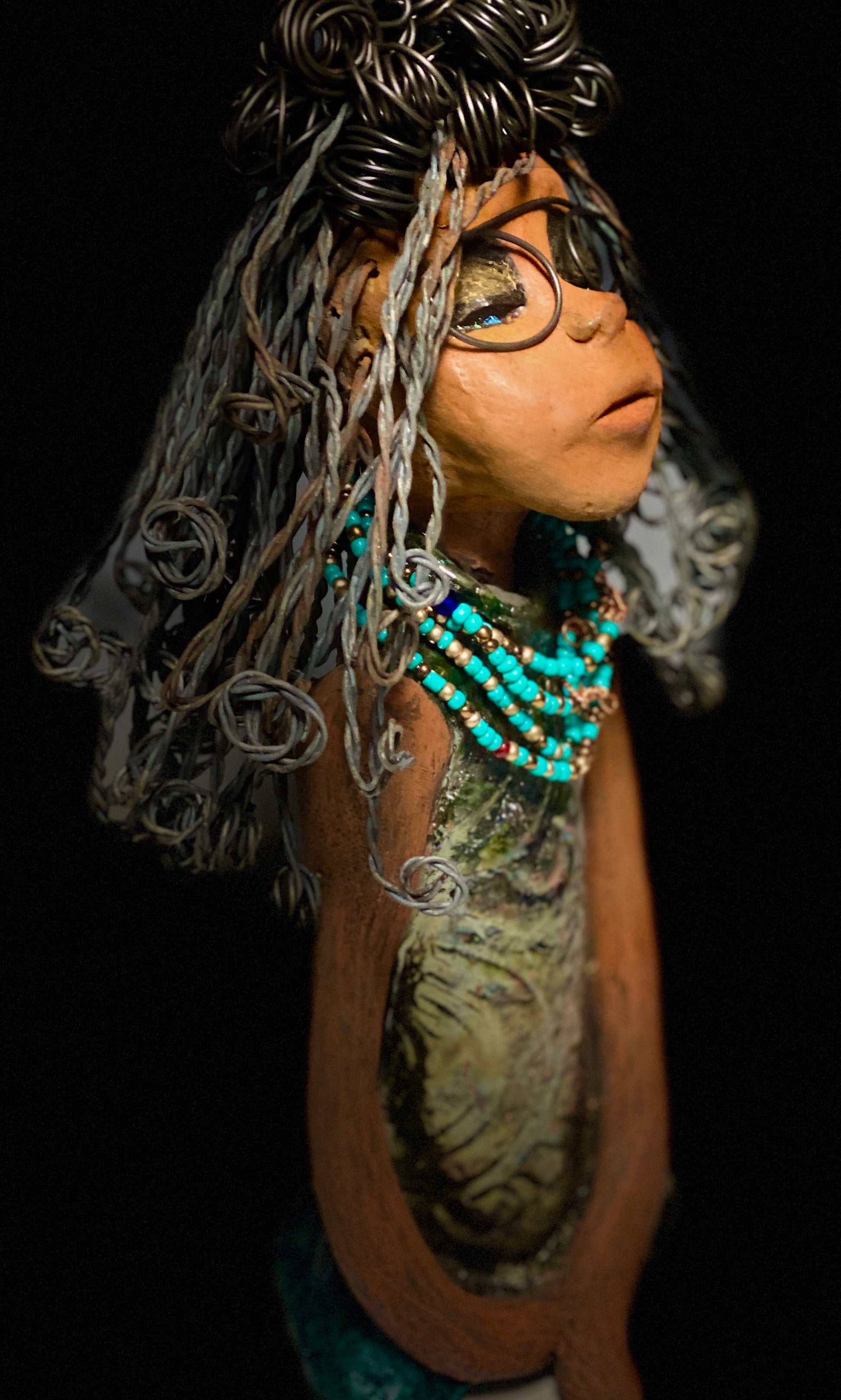 Meet Clarice! Clarice stand 13" x 6" x 5" and weighs 4.03 lbs. She has a lovely honey brown complexion with big bright eyes. Clarice wears glasses now! Her Herdew took over 2 hours to complete. It's made with 16 gauge wire. Clarice's dress is alligator green with streaks of copper. She has a blue beaded spiral necklace around her neck. Clarice looks to have a New ExtrArtindary Vision for 2021!
