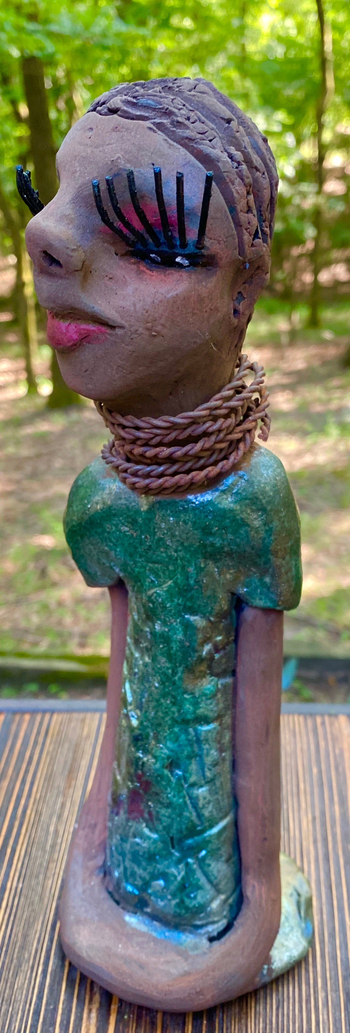 Meet  Ingrid Ingrid stands 12" x 5" x 4" and weighs 1.14 lbs. She has a lovely honey brown complexion with  reddish brown lips. She has a braided hairstyle.  Ingrid has a colorful metallic green antique copper glazed dress. She wears six spiral wire necklaces.  Her long loving arms rest at her sides. With long lashes and eyes slightly opened, Ingrid has hopes of finding a new home!