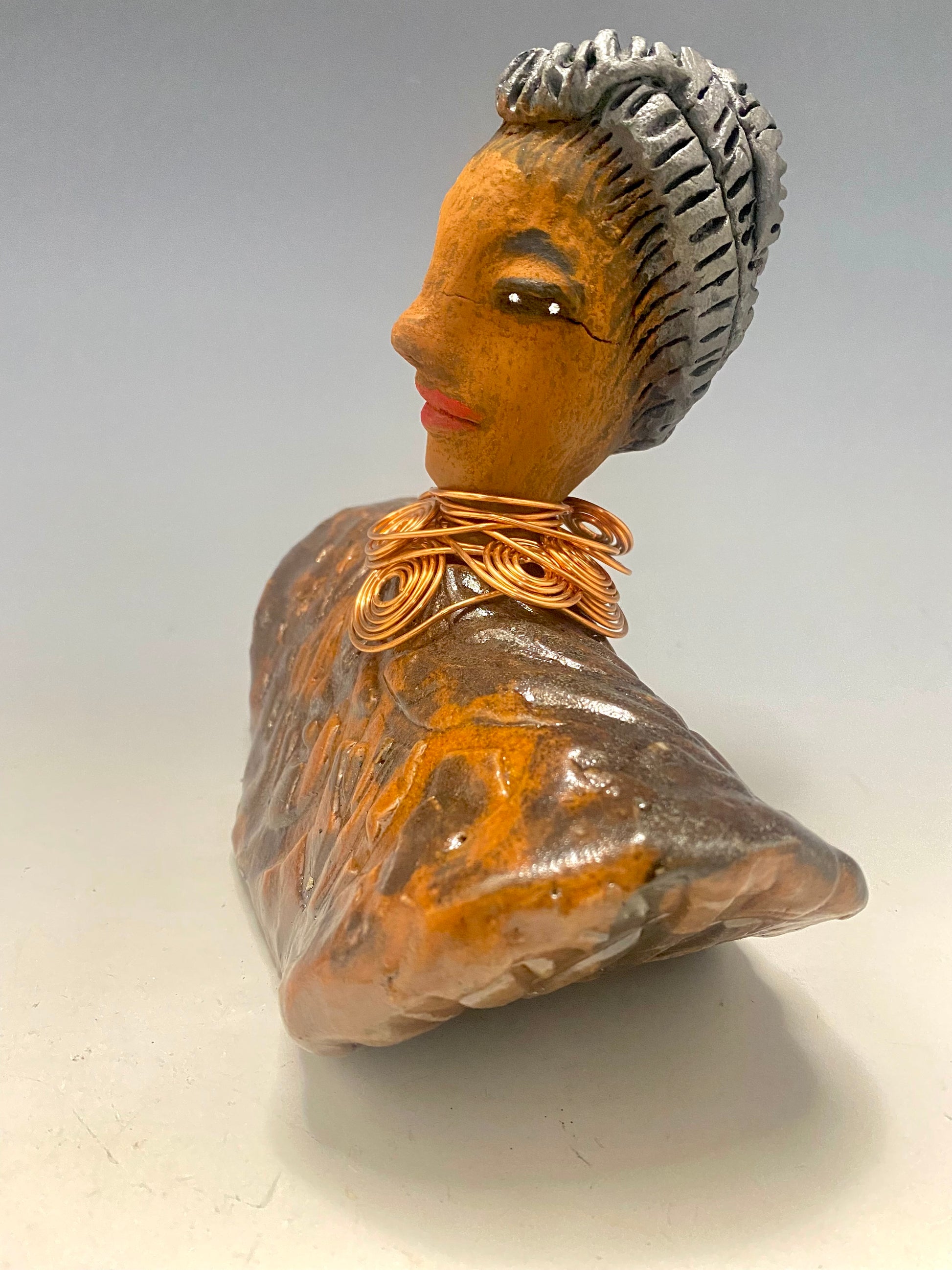 Meet Penny! Penny stands 8" x  8" x 3" and weighs 2.06 lbs. She has a lovely honey brown complexion. Penny has a metallic copper penny glaze on her textured robe. Her black eye shadow matches the black strands of baby hair around her edges. Penny's necklace has over 8 feetof spiral copper wire hair. Helen is somewhat angelic! Give Penny a prominent place in your home!