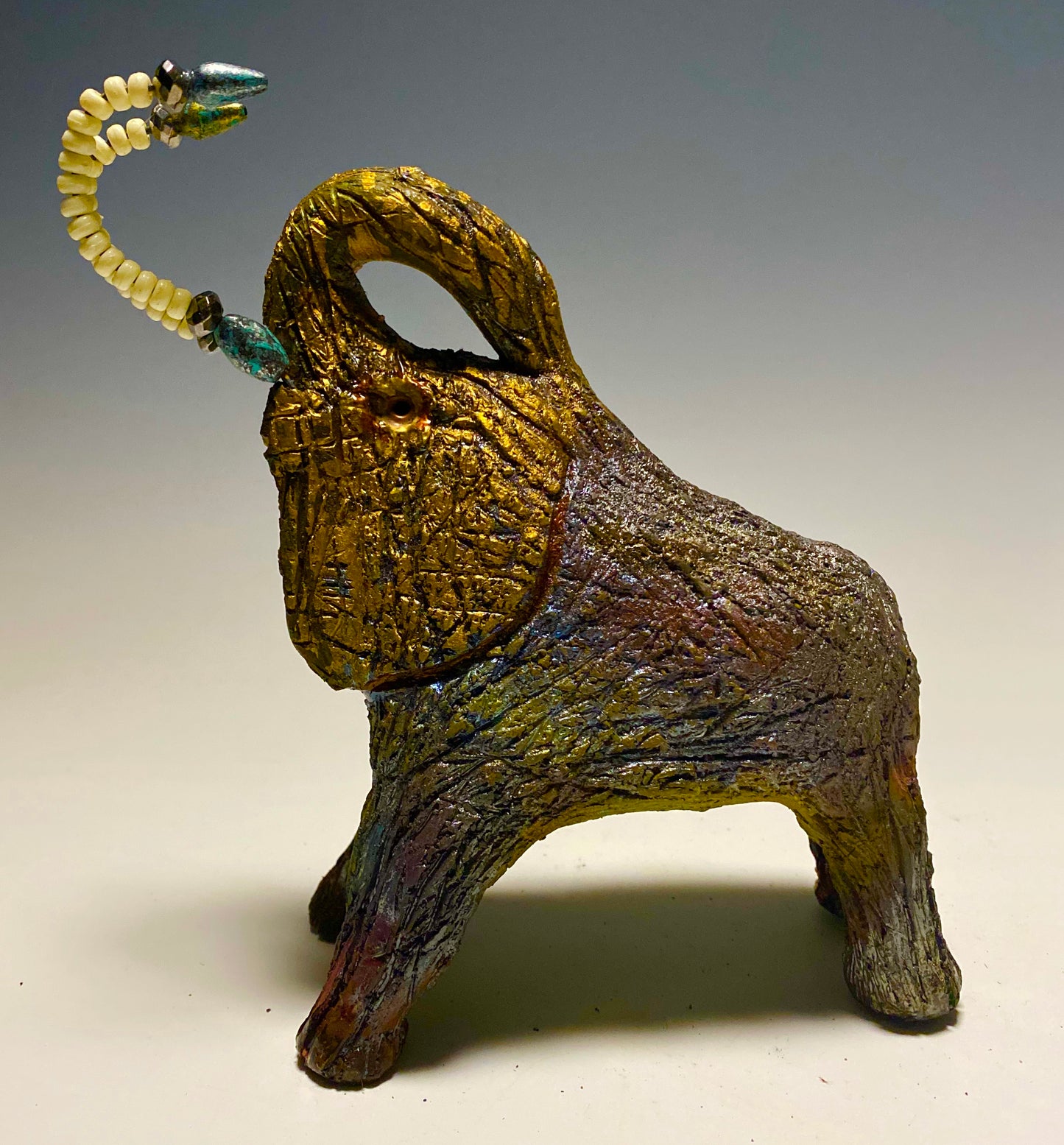 Raku Elephant Have you HERD!!!!!! Just one of these lovely Raku Fired Elephant will make an excellent gift for your friend, sorority or for your home’ special place centerpiece. 7" x 4" x 4" 1.3 lbs White beaded with silver and blue tusk Beautiful metallic raku colors For decorative purposely only.