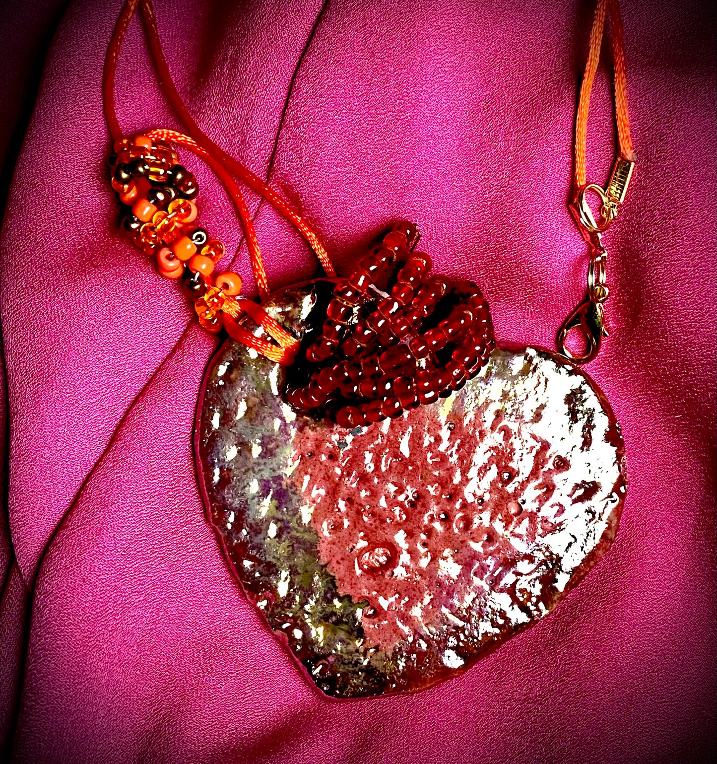 Have A Heart ! Each heart pendant is handmade with love! It is 3"x 3" and weighs approx. 3ozs. This pendant has a red violet and gold metallic raku glazes that renders a unique translucent patina. The heart has a textured pattern . Both sides are are different and equally beautiful! It holds a spiral of red violet mini beads on a spiral copper wire. This pendant has a nice 12" red suede cord!