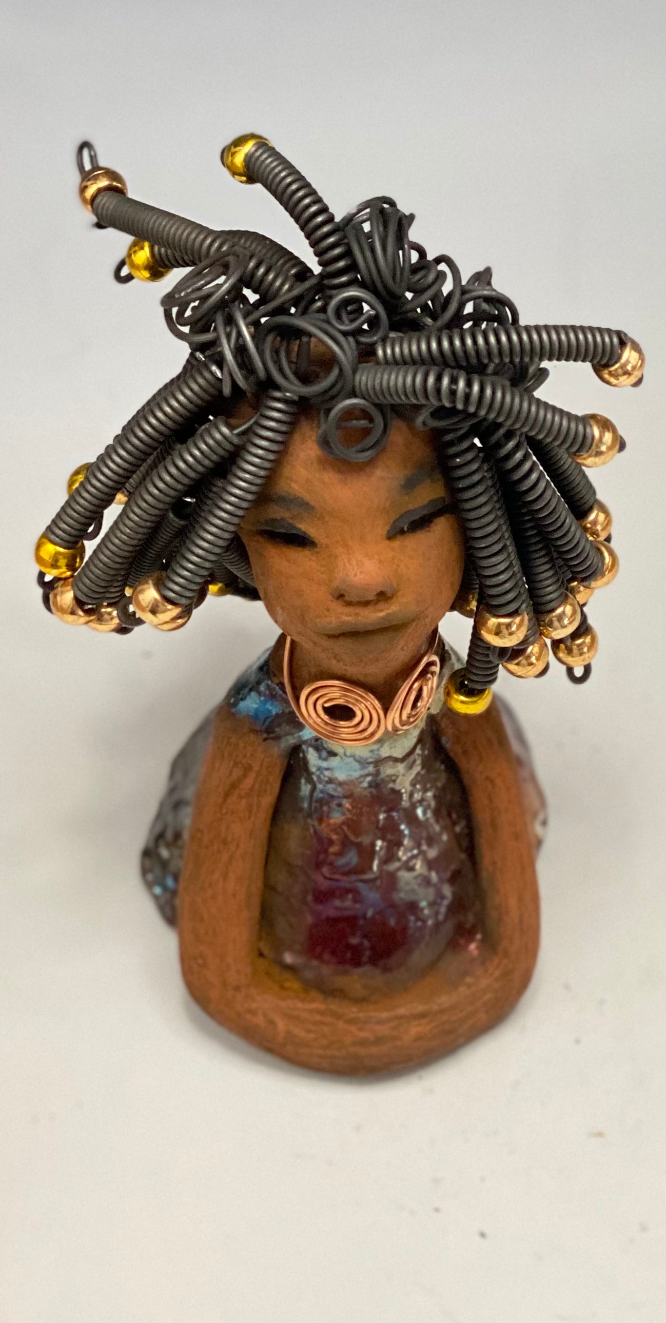 Meet Alexus Alexus stands 7.5" x 4" x 4" and weighs 1.05 lbs. She wears a lovely glossy metallic gold dress adorn by a spiral copper necklace. Alexus has over15 feet of coiled wire hair with gold beads.. Alexus appears to sit in a yoga pose. Her long arms rest at her side. Alexus is a great starter piece from the Herdew Collection!