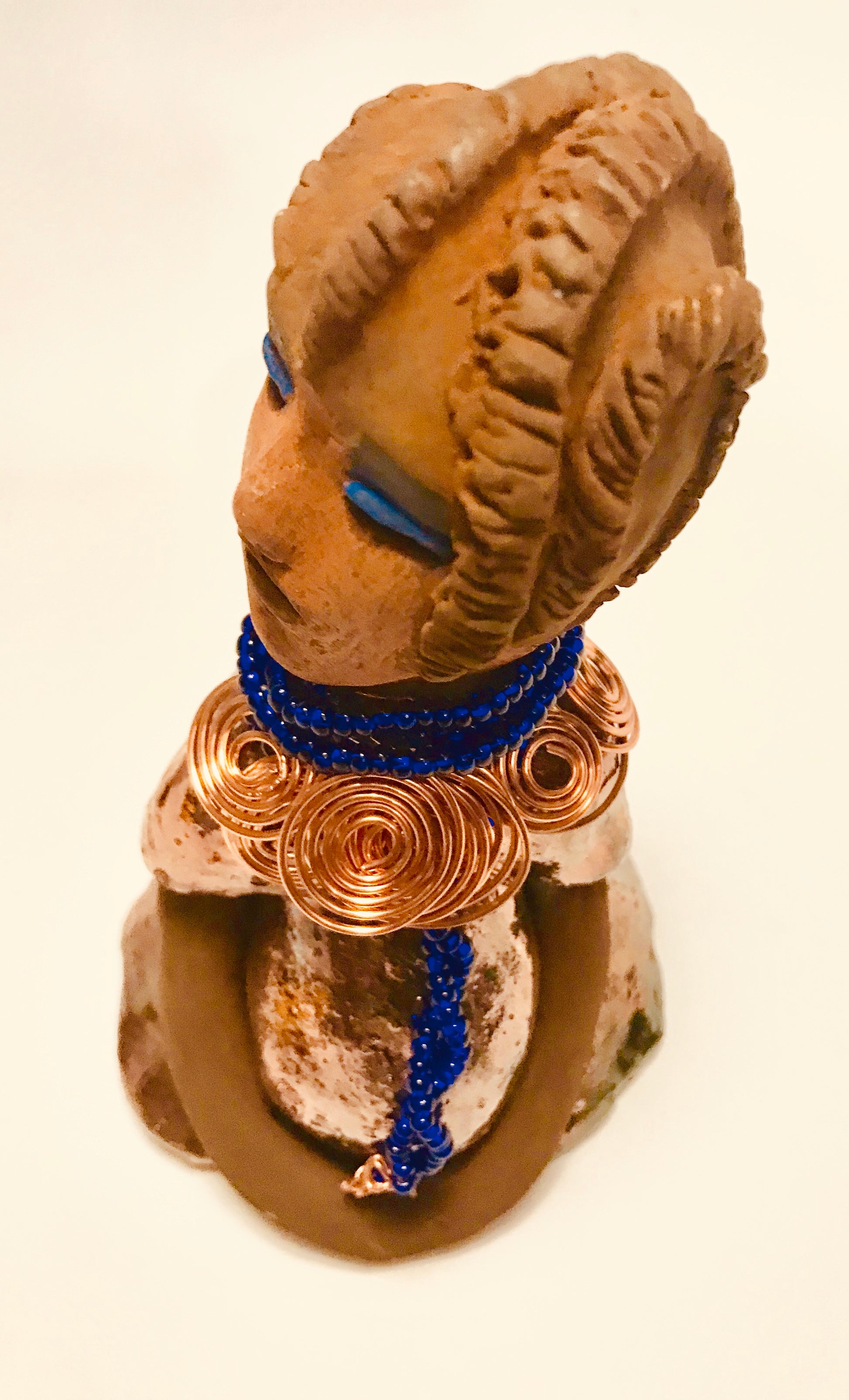 Ife stands 7.5" x 4" x 5" and weighs 1.02  lbs. She has a lovely honey brown complexion with reddish brown lips. She has a short braided hairstyle.      Ife has a colorful metallic antique copper glazed dress.     She wears spiral copper wire necklaces on top of an aqua blue beaded collar.     Ife long loving arms rest at her side.     With accent blue eye shadow and eyes wide opened, Ife has hopes of finding a new home.