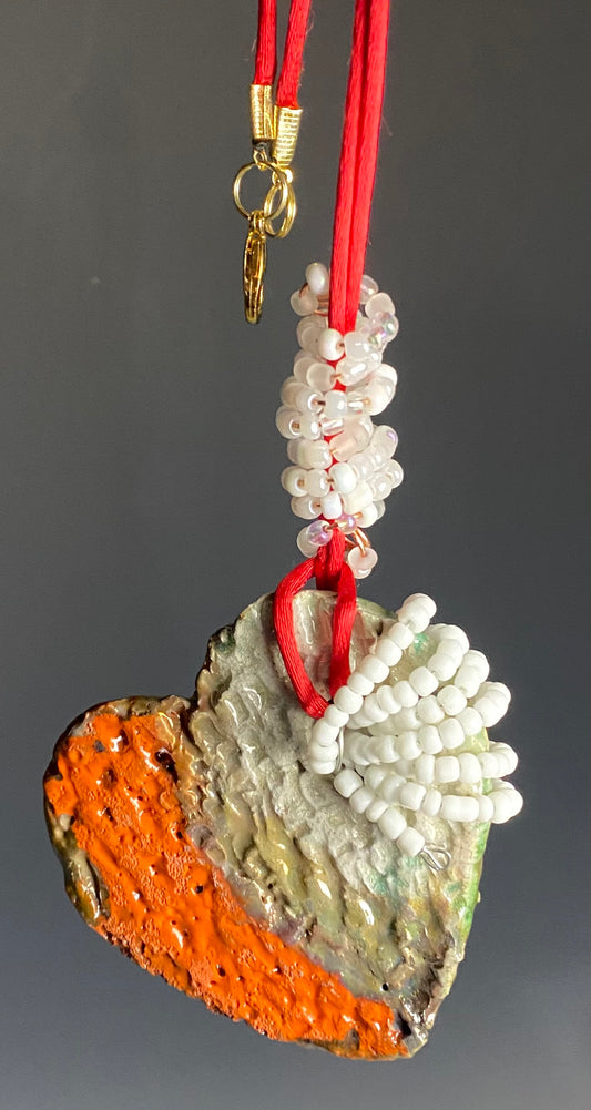 Have A Heart ! Each heart pendant is handmade with love! It is 3"x 3" and weighs approx. 3ozs. This pendant has a orange gold metallic raku glazes that renders a unique translucent  patina. The heart has a textured pattern . It holds a spiral of white and clear mini beads on a spiral copper wire. This pendant has a nice 12" red suede cord!