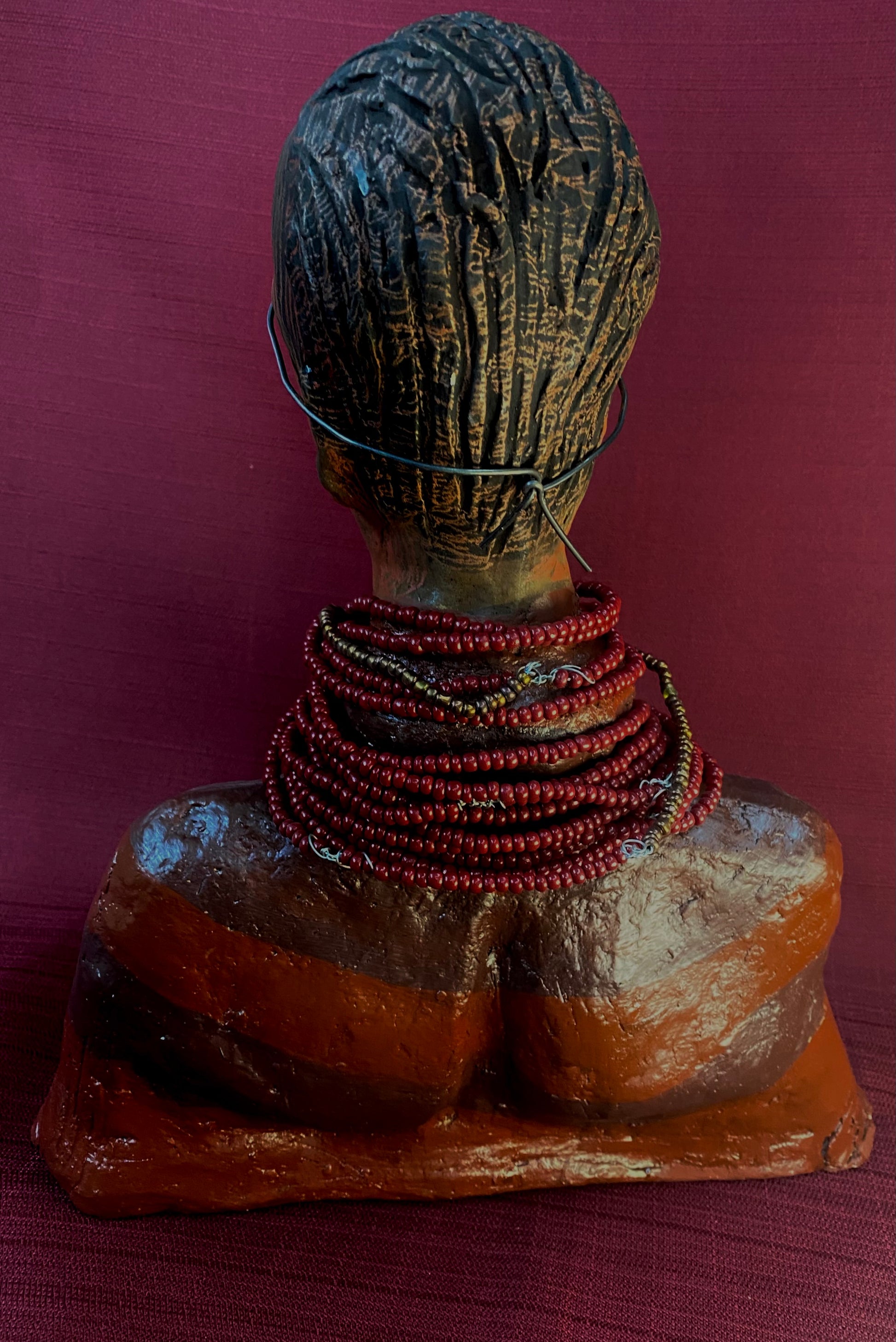 Meet Harriet! Harriet stands 13" x 11" x 5" and weighs 5 lbs. She wears a coral striped dress with a string of ruby red and gold beads. Harriet has a honey brown rust complexion  and distinct eyes. Her eyes  are slightly opened underneath her glasses... She has mixed black and copper streaks of straight corn rolls of clay hair. She has a straight look of concern as to what is about to take place.