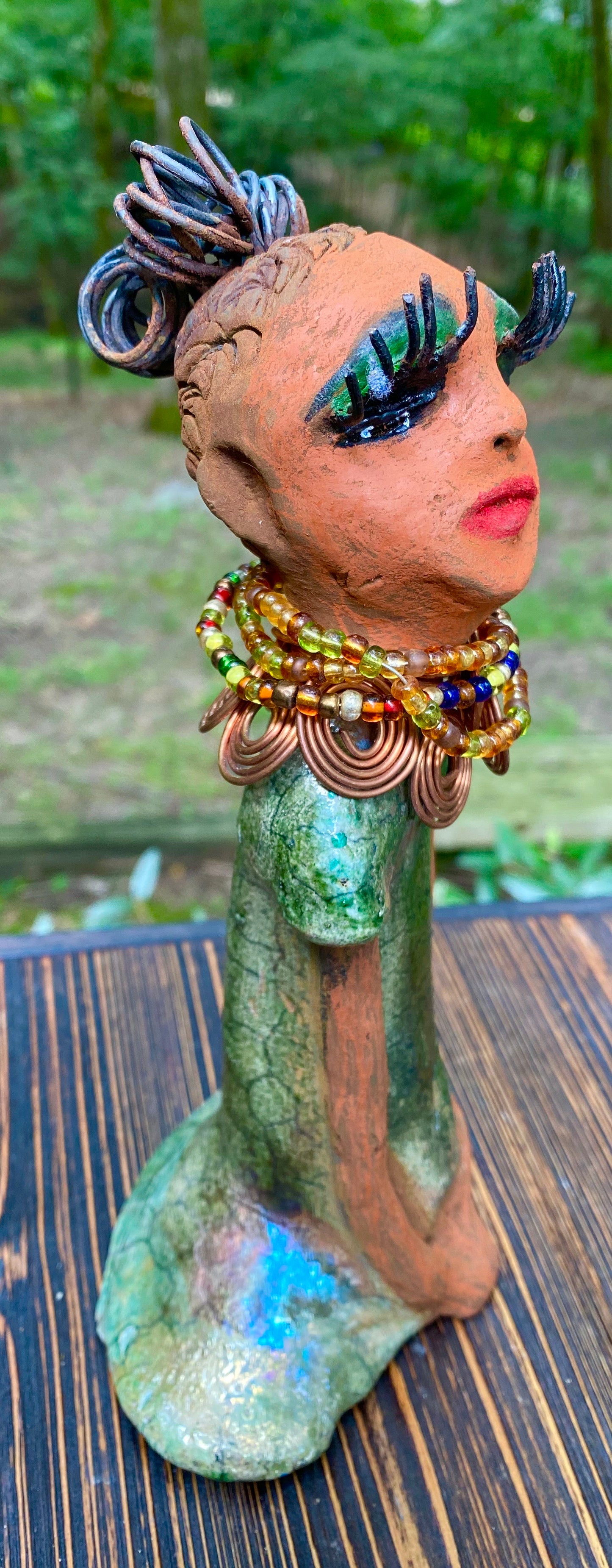 Kaleesia says yes to wire hair and yes to the Herdew tribe. Kaleesia stands 9” x 5" x 2.5" and weighs 1.05 lbs. She has a lovely beige brown complexion with short etched braided clay hair. Kaleesia long loving arms rest beside her multicolored copper green dress. Kaleesia is a sophisticated lady that will grace your home.